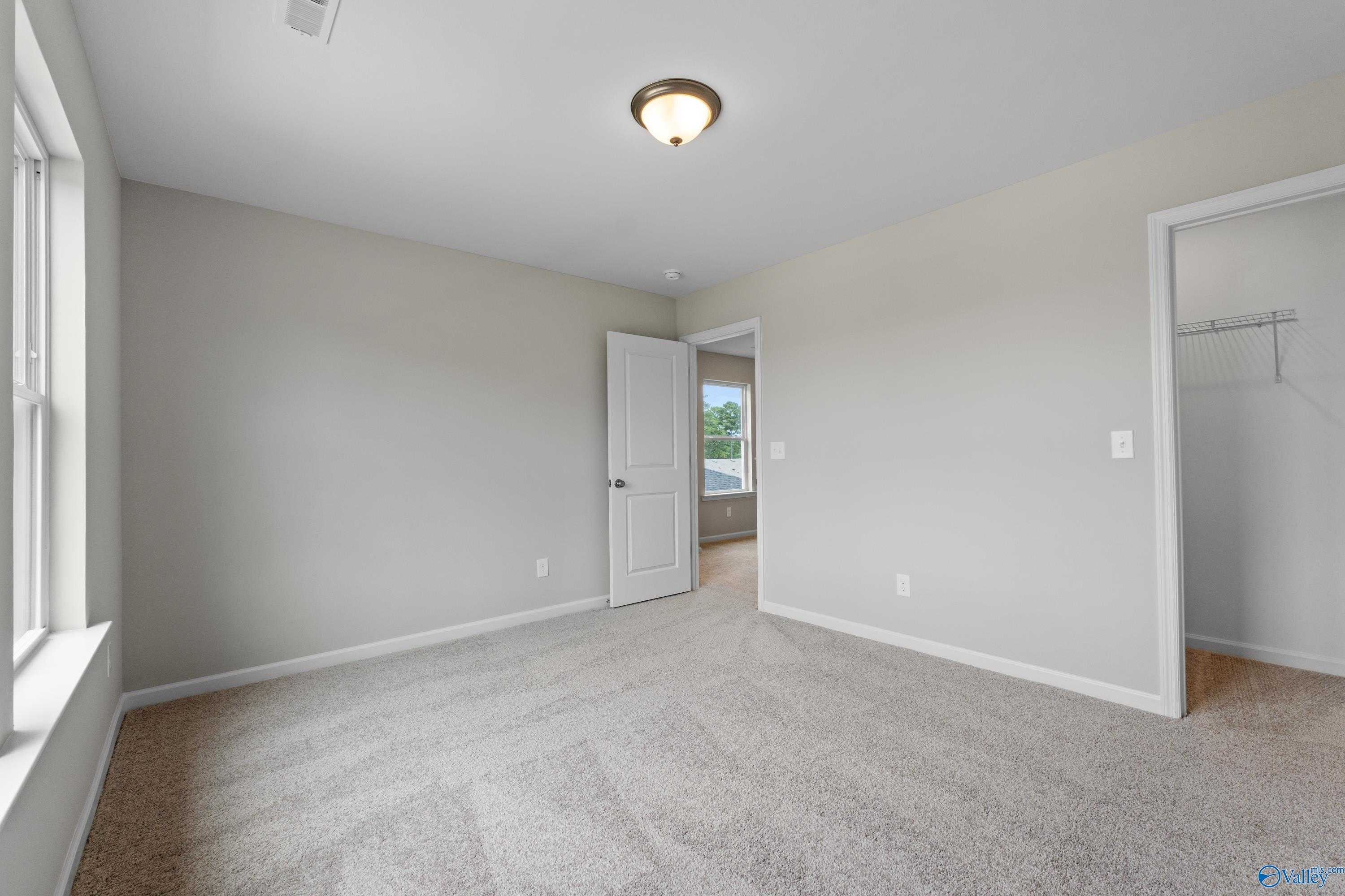 Spacious secondary bedroom featuring neutral beige walls, plush carpet, and adjacent closet in Evermore Homes The Augusta, Madison Alabama