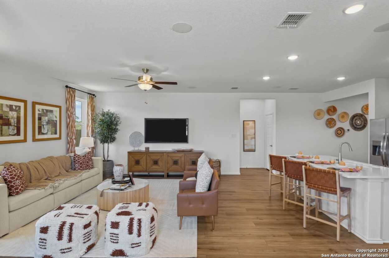 Cozy open living room with beige sectional sofa, leather armchair, TV credenza, and bar stools in The Daphne J by Davidson Homes, Elmendorf, Texas