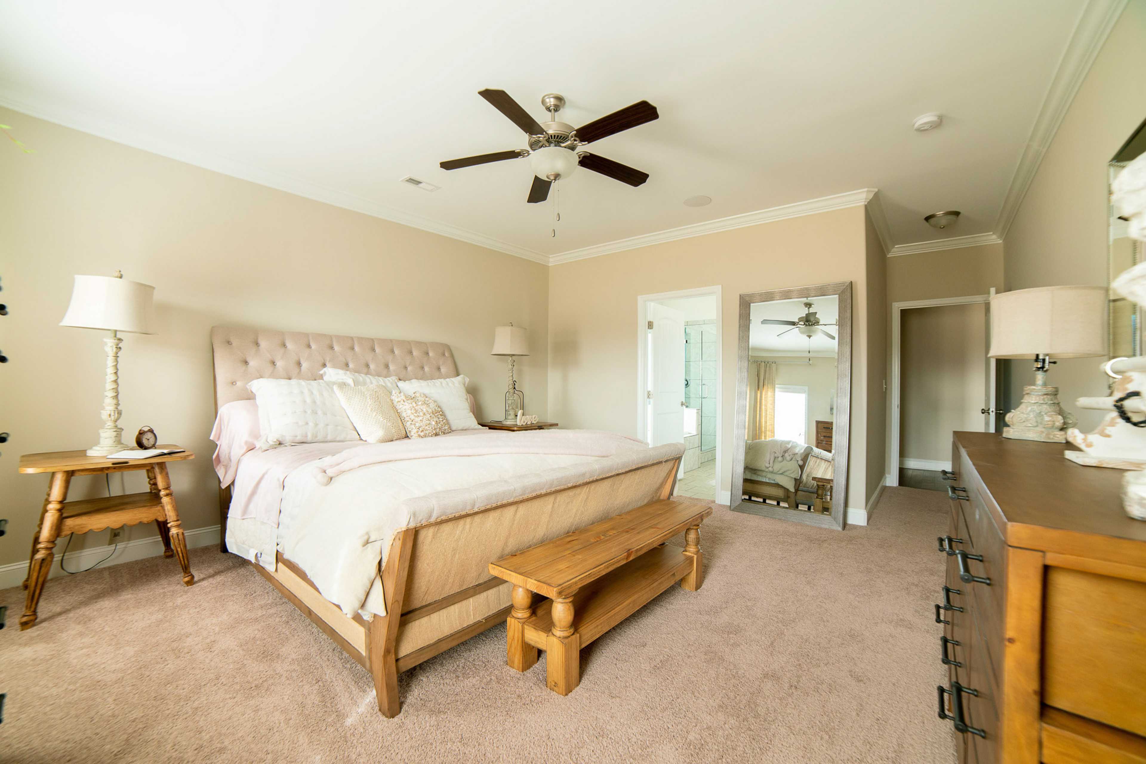 Spacious master bedroom at The Dairy at Oak Grove in South Huntsville AL with beige walls, upholstered bed, ceiling fan, and wooden bench