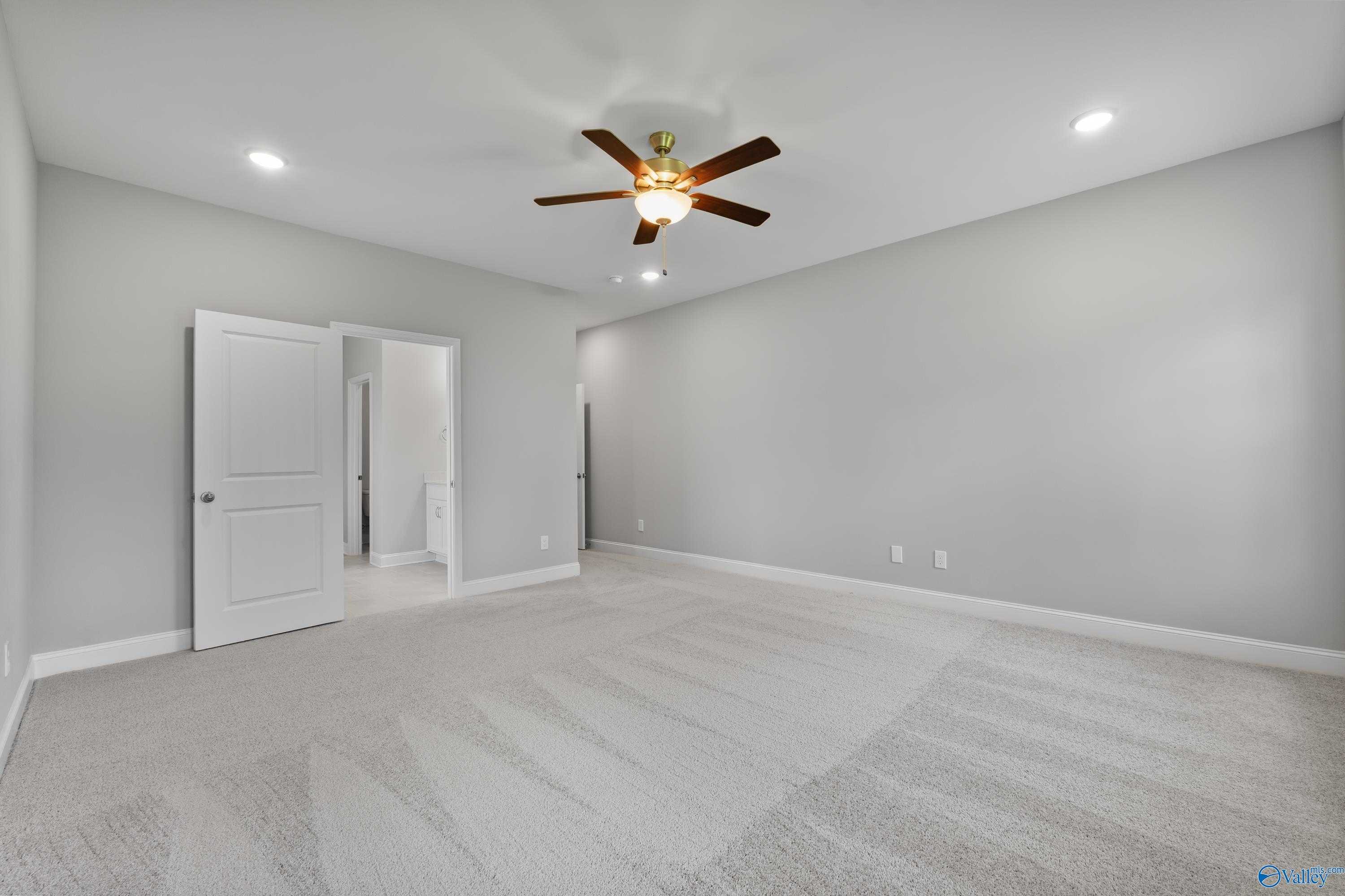 Spacious master bedroom with gray walls, ceiling fan, recessed lights, and open doors in Davidson Homes The Rockford, Harvest, AL