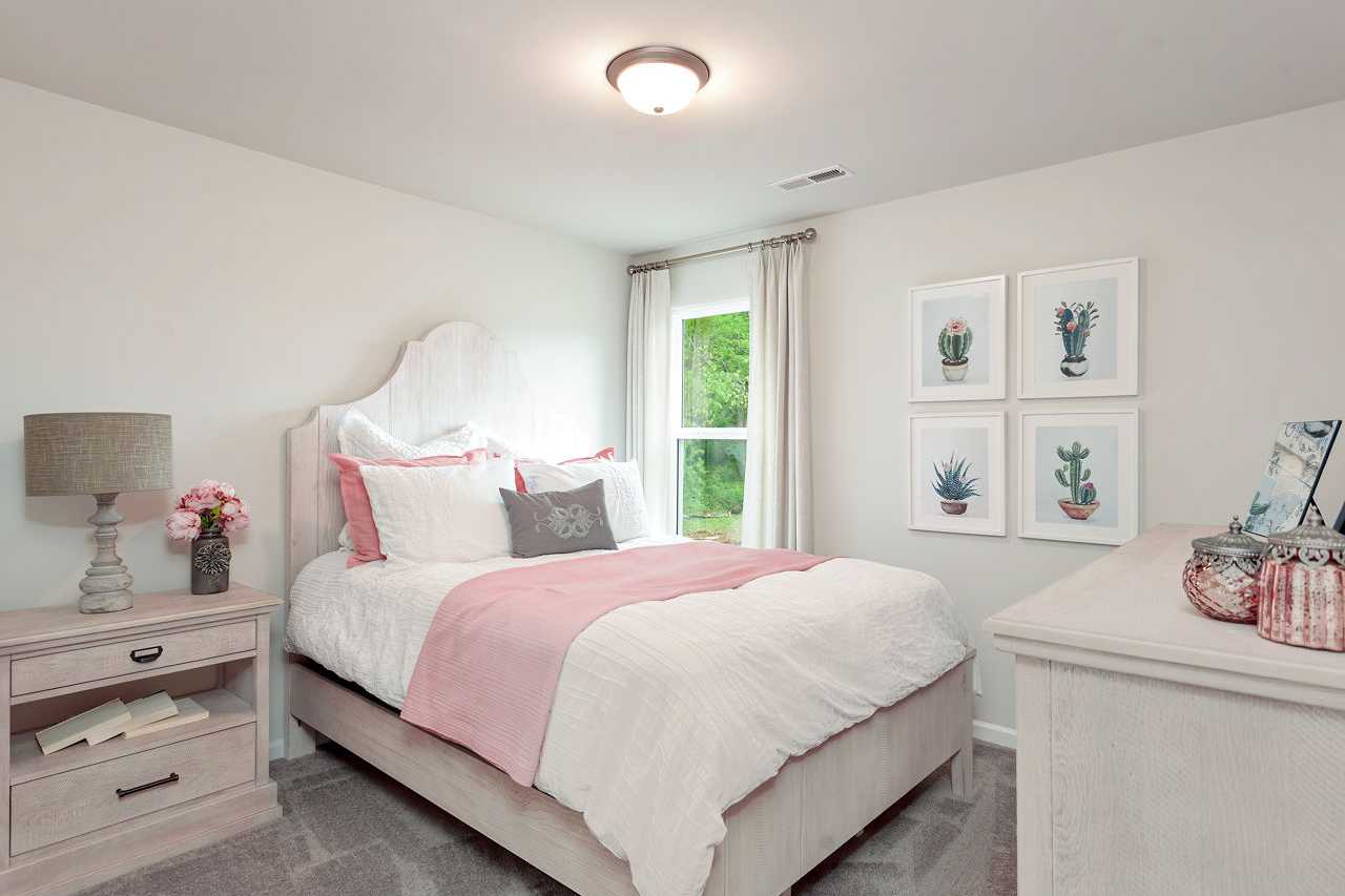 Cozy secondary bedroom in The Franklin home design with pink bedding, tufted headboard, succulent art, and window view