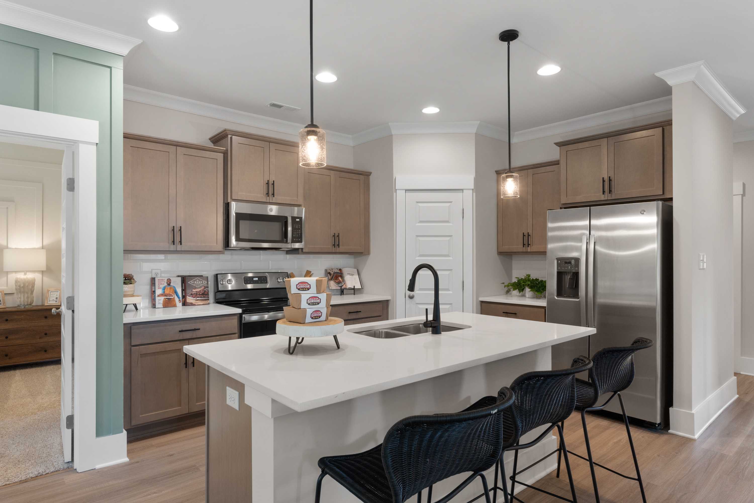 Modern kitchen at Hollon Meadow in Decatur Alabama with light wood cabinets, white quartz island, black stools, and stainless steel appliances