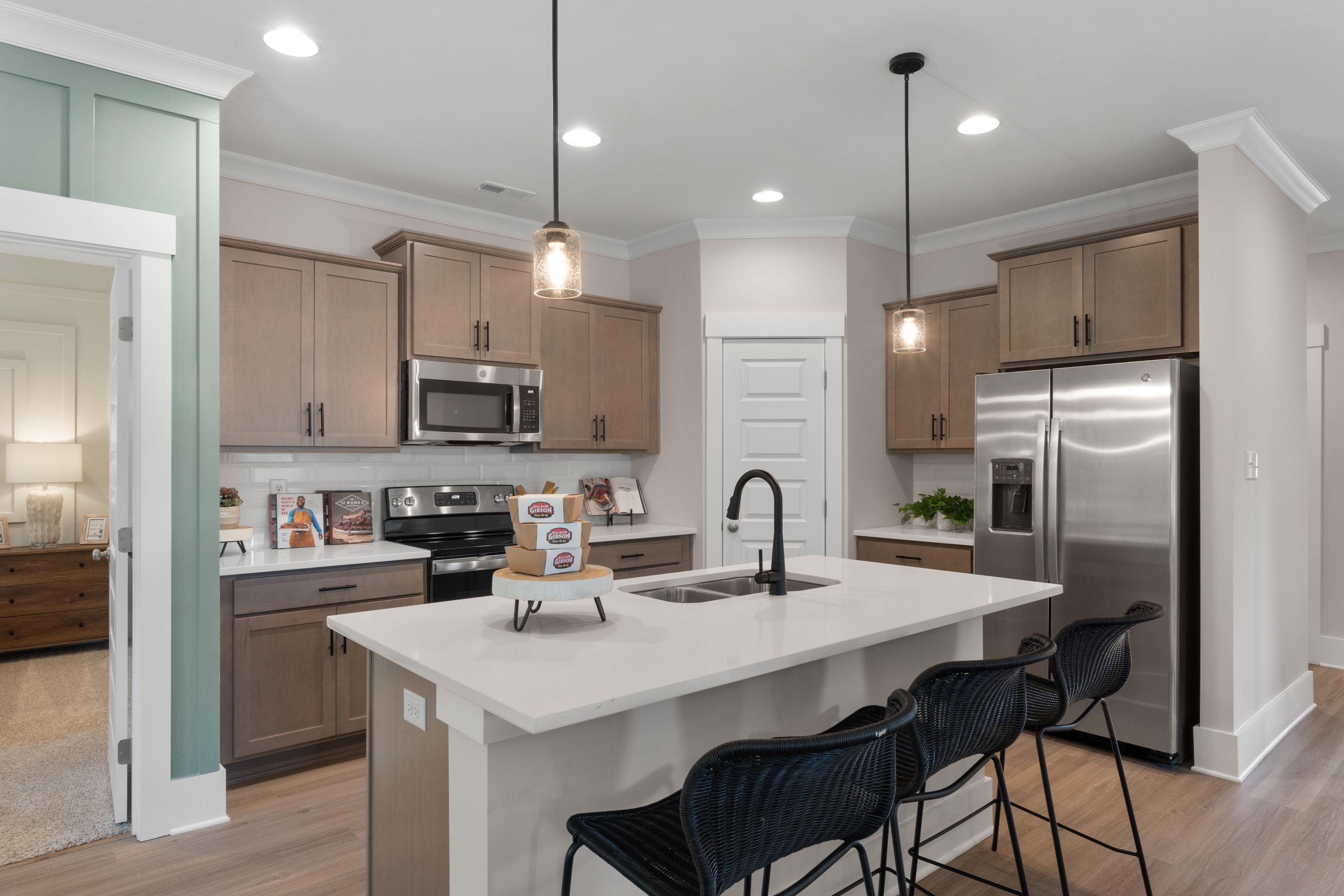 Modern kitchen at Hollon Meadow in Decatur Alabama with light wood cabinets, white quartz island, black stools, and stainless steel appliances