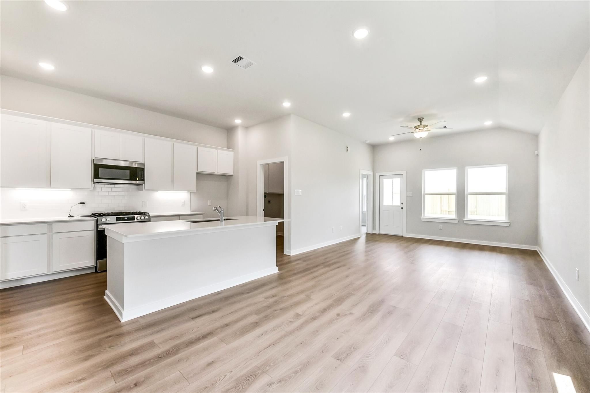 Bright open-concept kitchen with white island, stainless appliances, and hardwood floors in Davidson Homes The Costa B, Dayton, Texas