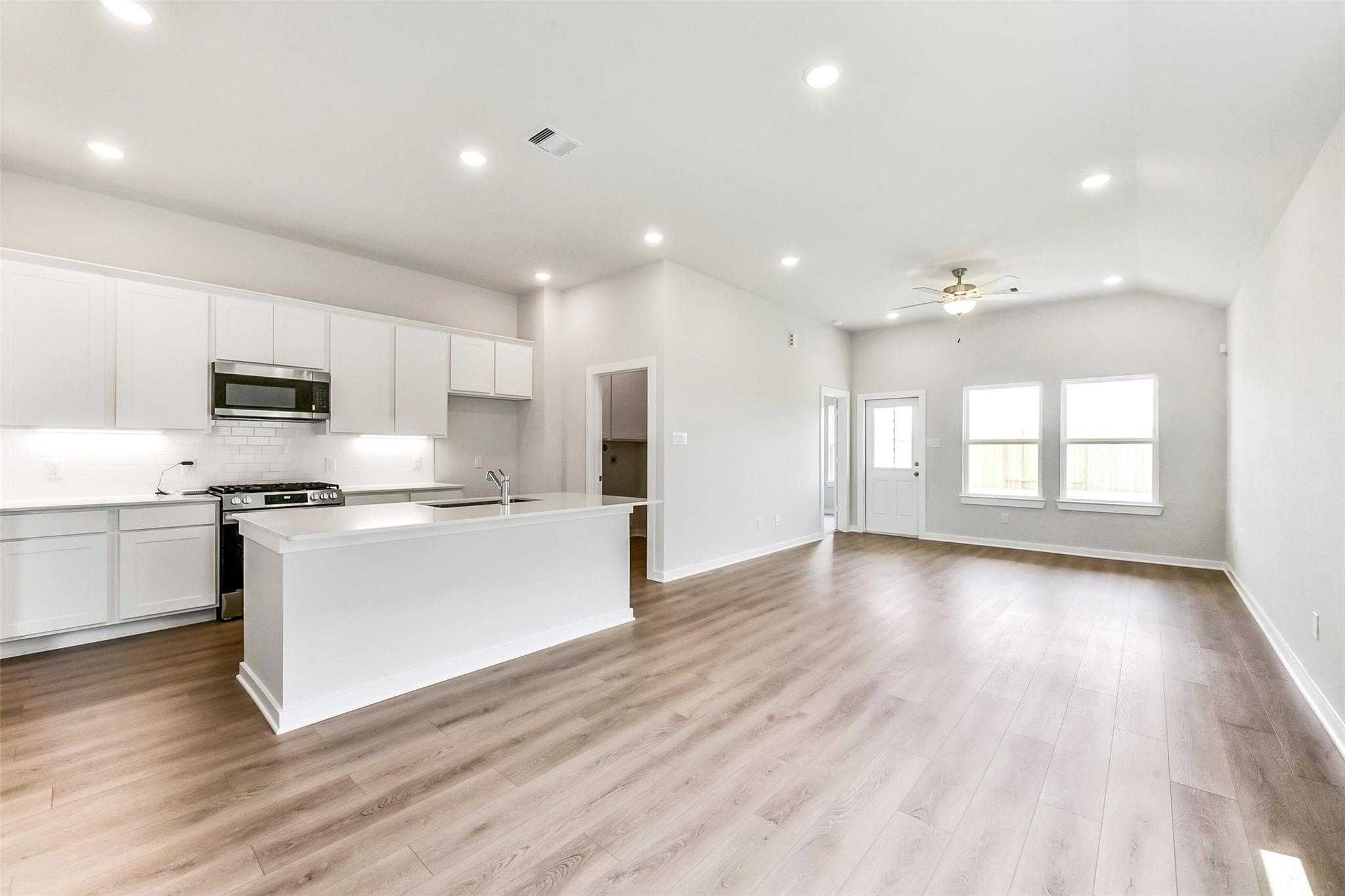 Bright open-concept kitchen with white island, stainless appliances, and hardwood floors in Davidson Homes The Costa B, Dayton, Texas