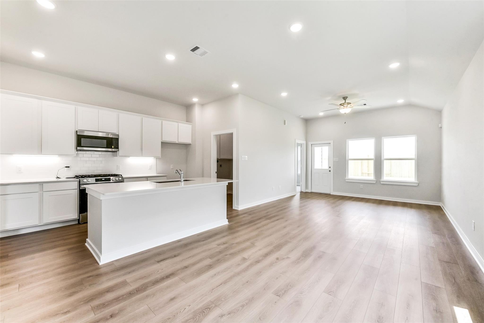 Modern open-concept kitchen with white island, stainless appliances, and hardwood floors in The Costa B 3-car garage home, Dayton, Texas