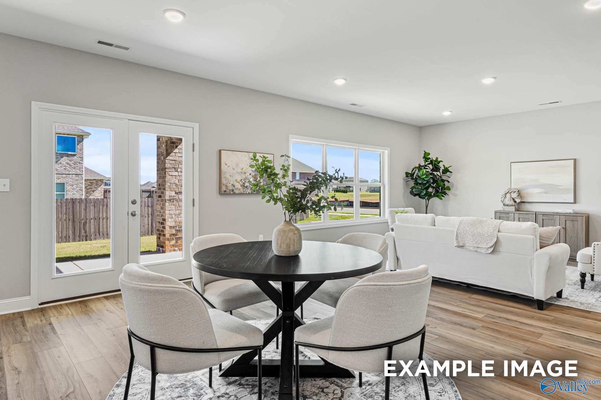 Bright living room with round black table, beige chairs, white sofa, French doors to backyard in Davidson Homes Chelsea B, Toney, AL