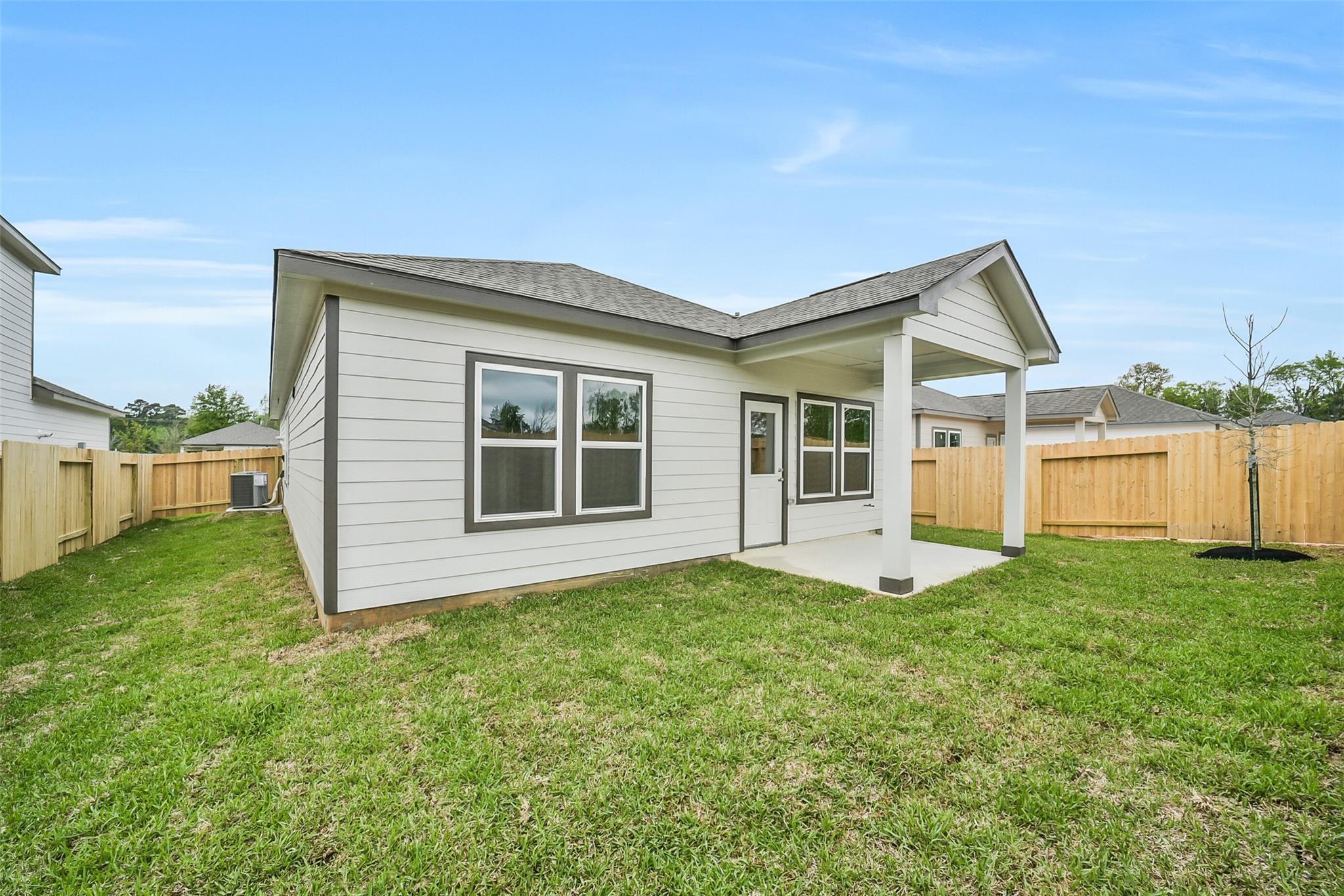 Rear view of single-story The Frio F home by Davidson Homes with covered patio, fenced yard, and lush grass in Caney Creek Place, Conroe, Texas