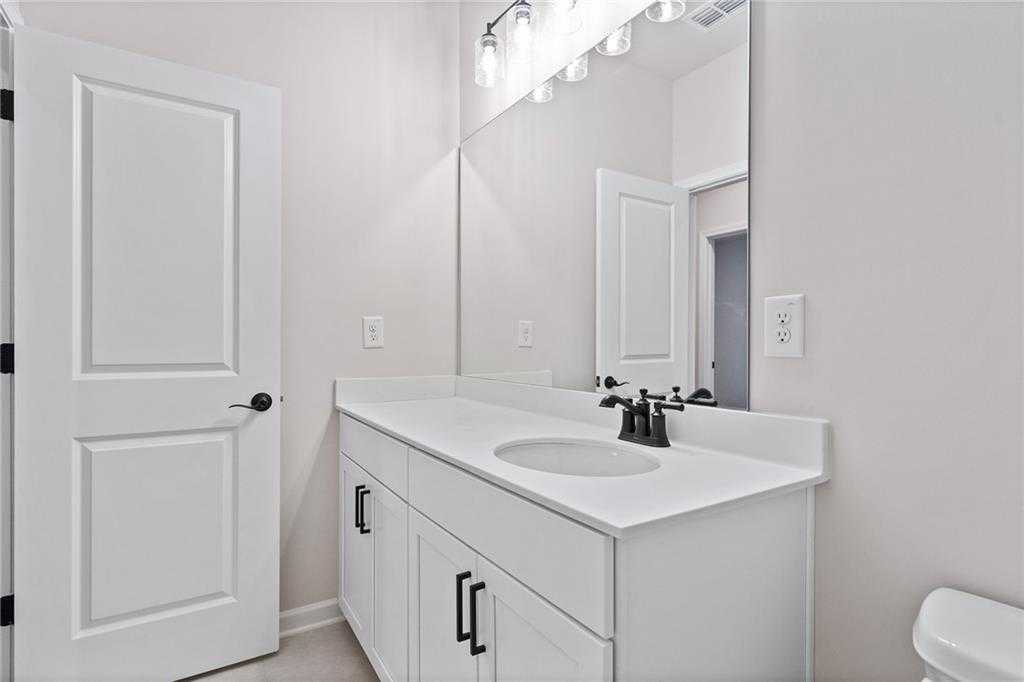 Bright bathroom with white vanity, undermount sink, chrome faucet, and large mirror in The Glenwood C home, Loganville, Georgia