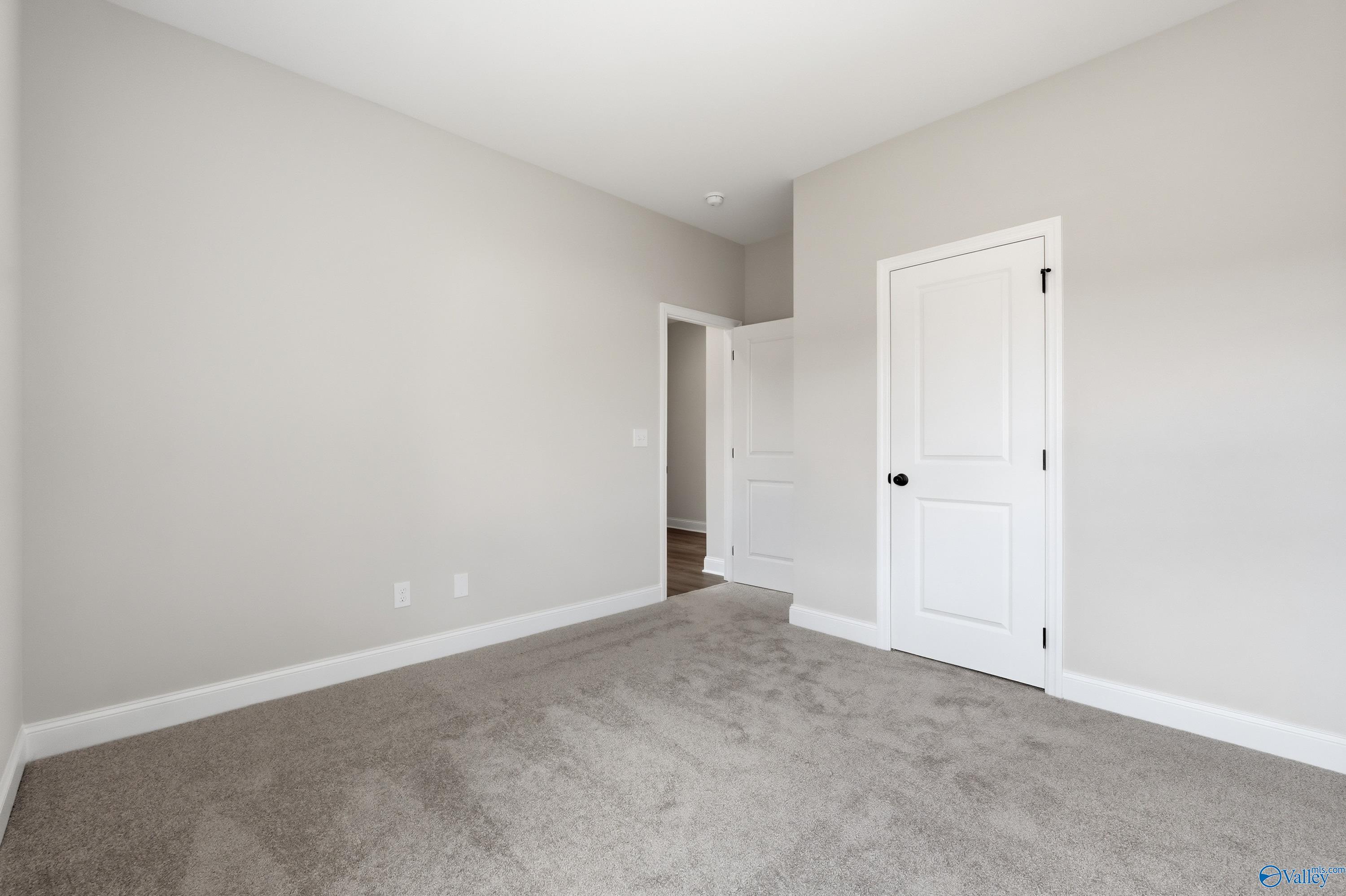 Spacious empty bedroom with gray carpet, light gray walls, white doors in Davidson Homes The Franklin C, Meridianville, Alabama