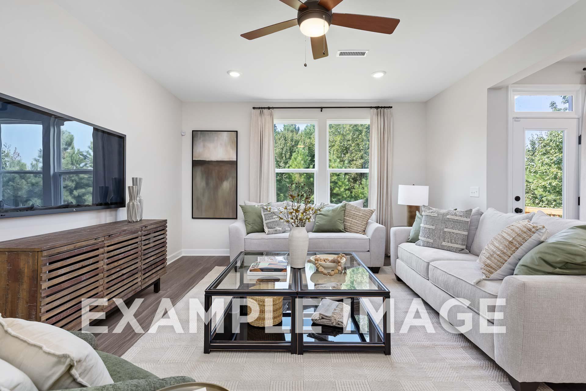 Bright living room in The Willow E by Davidson Homes featuring white L-shaped sofa, glass coffee table, wall TV, and large windows