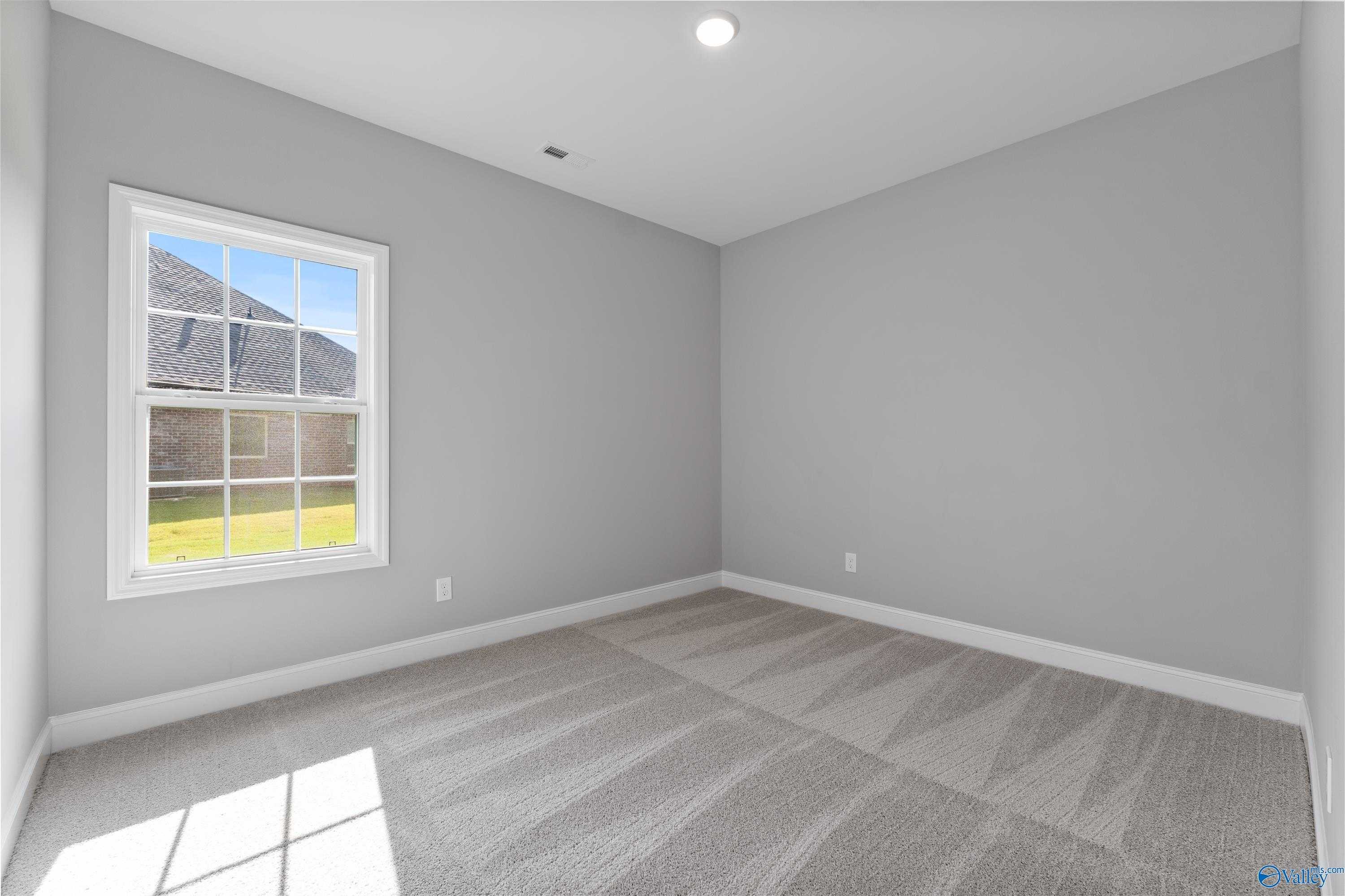 Sunlit secondary bedroom with gray walls, large window overlooking lawn, plush carpet in Davidson Homes The Rockford, Harvest, Alabama