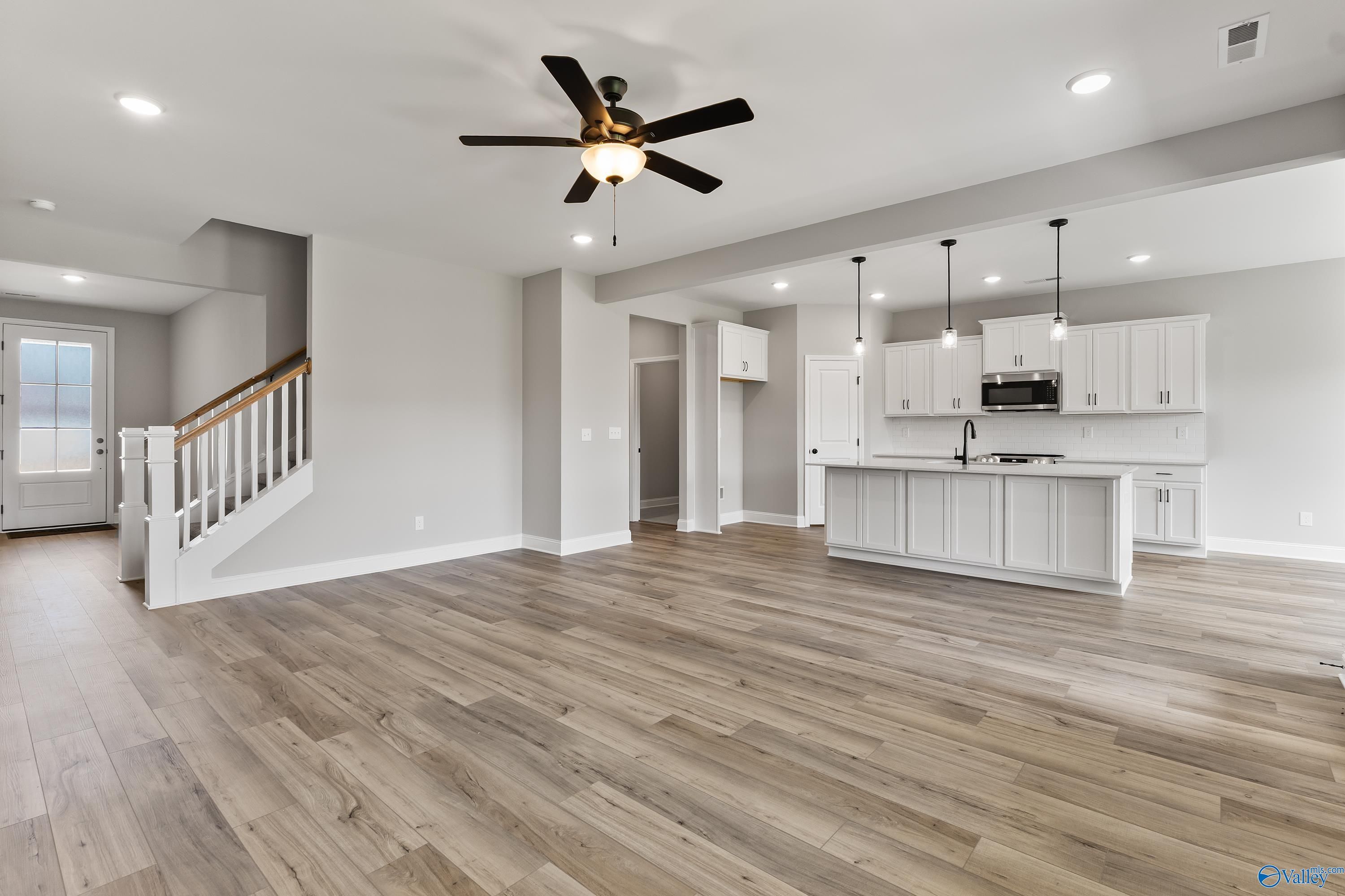 Open-concept kitchen and living area with white island, hardwood floors, ceiling fans, and staircase in Davidson Homes Montgomery B With Bonus, Toney, AL