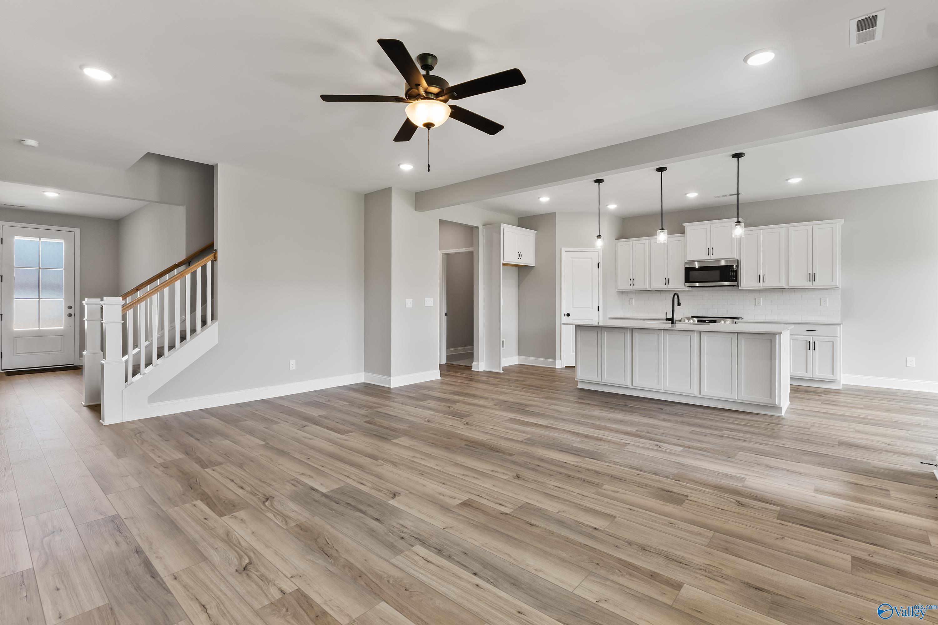 Open-concept kitchen and living area with white island, hardwood floors, ceiling fans, and staircase in Davidson Homes Montgomery B With Bonus, Toney, AL