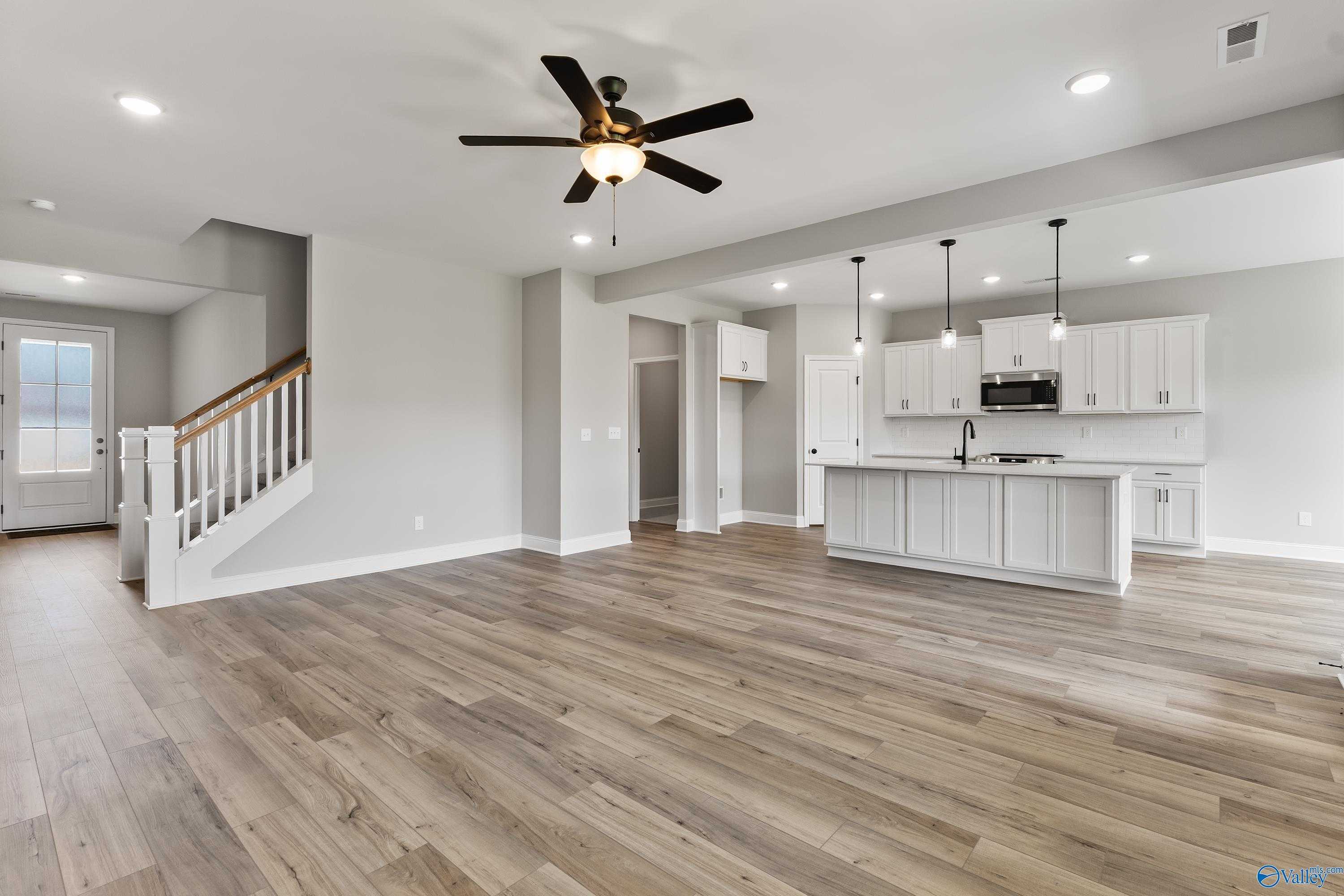 Open-concept kitchen and living area with white island, hardwood floors, ceiling fans, and staircase in Montgomery B With Bonus, Toney AL