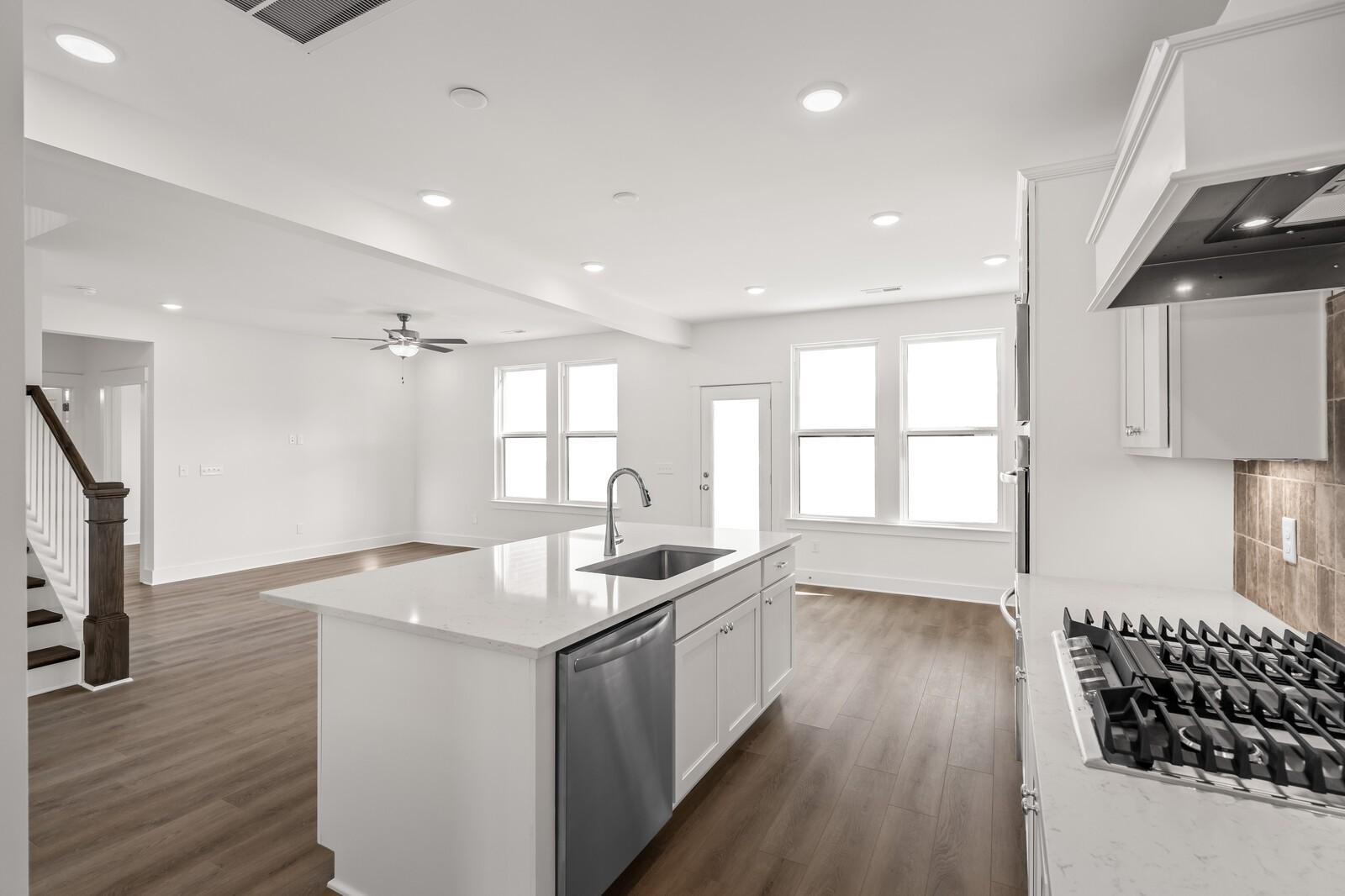 Modern open-concept kitchen with white island sink, stainless dishwasher, gas range, hardwood floors, and large windows in The Willow D home, Mt. Juliet, TN