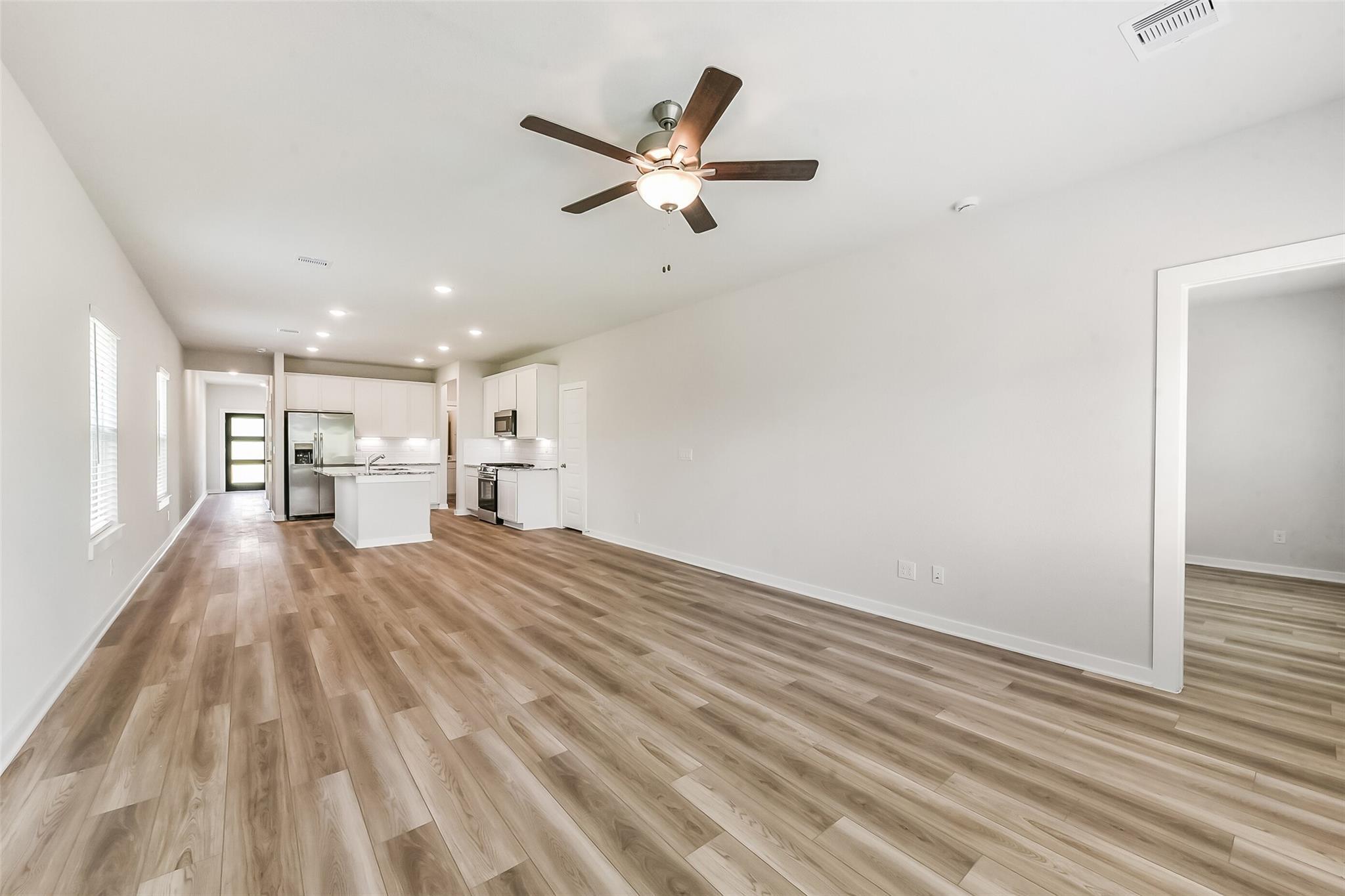 Open-concept kitchen and living area with white shaker cabinets, stainless steel appliances, and hardwood-look flooring in The Frio G, Magnolia, TX