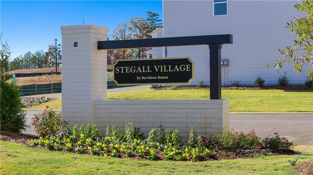 Elegant Stegall Village entrance sign by Davidson Homes in Emerson, Georgia, featuring white brick pillars, vibrant flowers, and lush greenery