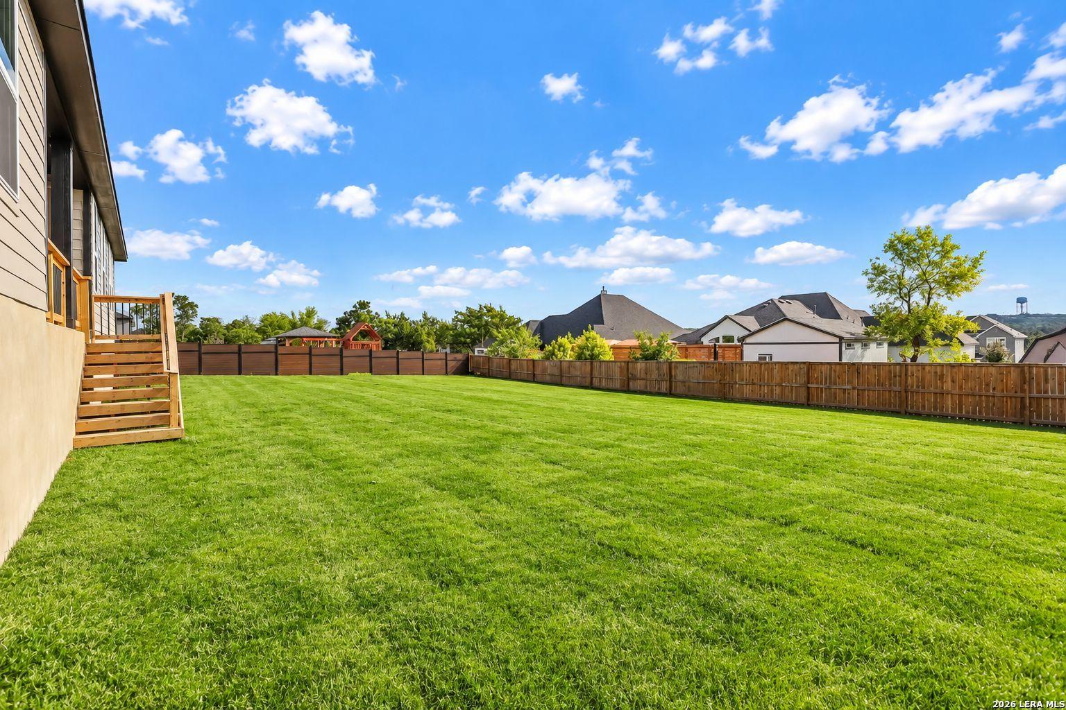 Spacious fenced backyard with lush green lawn and wooden stairs in Davidson Homes The Foster E, Potranco Oaks, Castroville, Texas