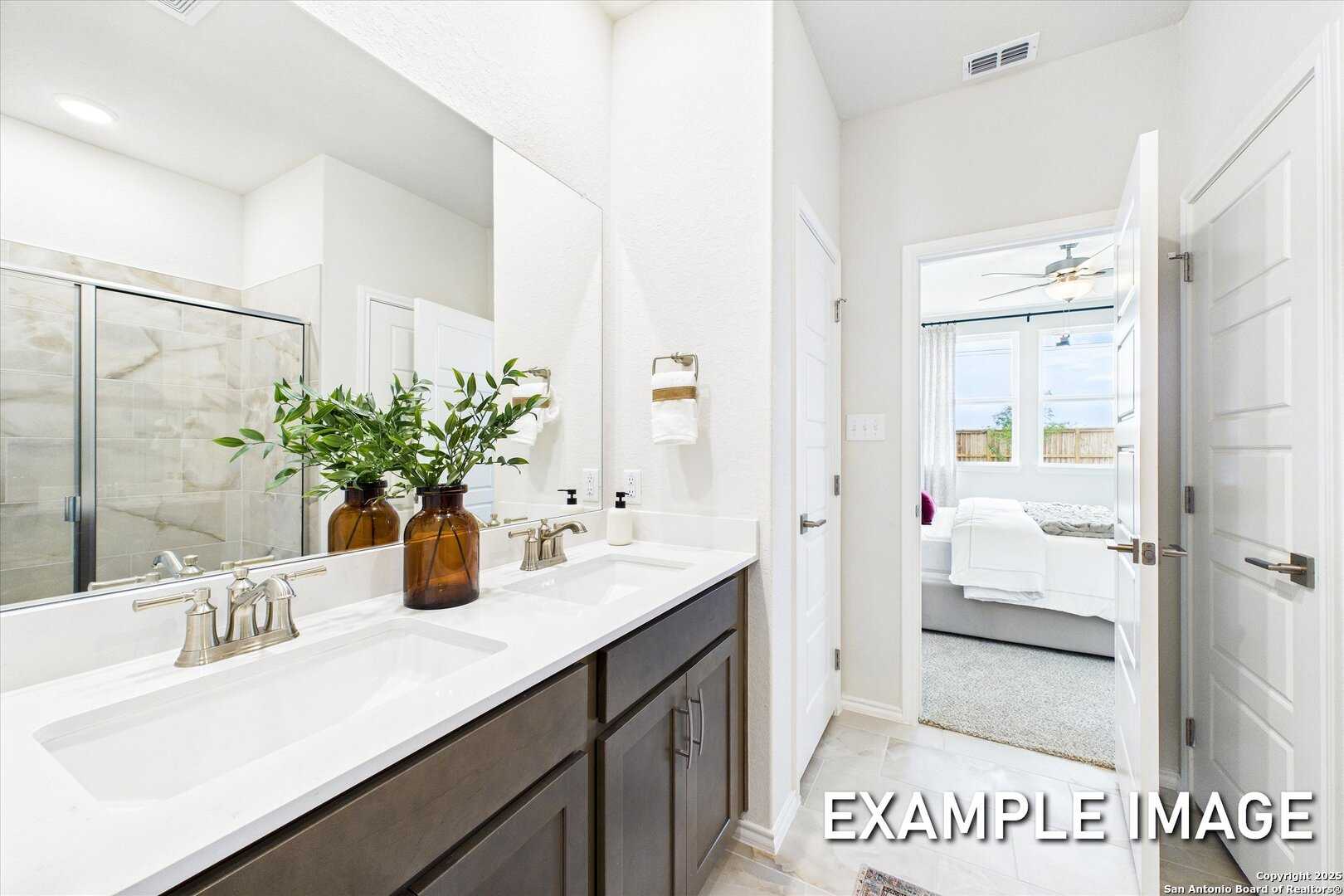 Modern master bathroom with double vanity, glass shower, plants, and bedroom view in The Brazos C, Davidson Homes, San Antonio