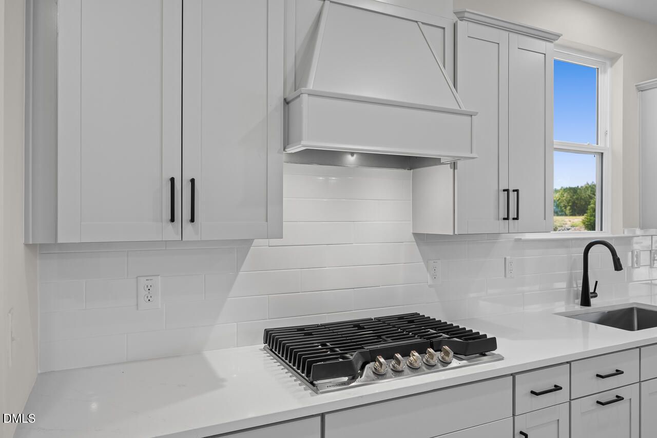 Modern white kitchen with gas cooktop, range hood, and black faucet in Davidson Homes Ashport M plan, Wendell Ridge, NC