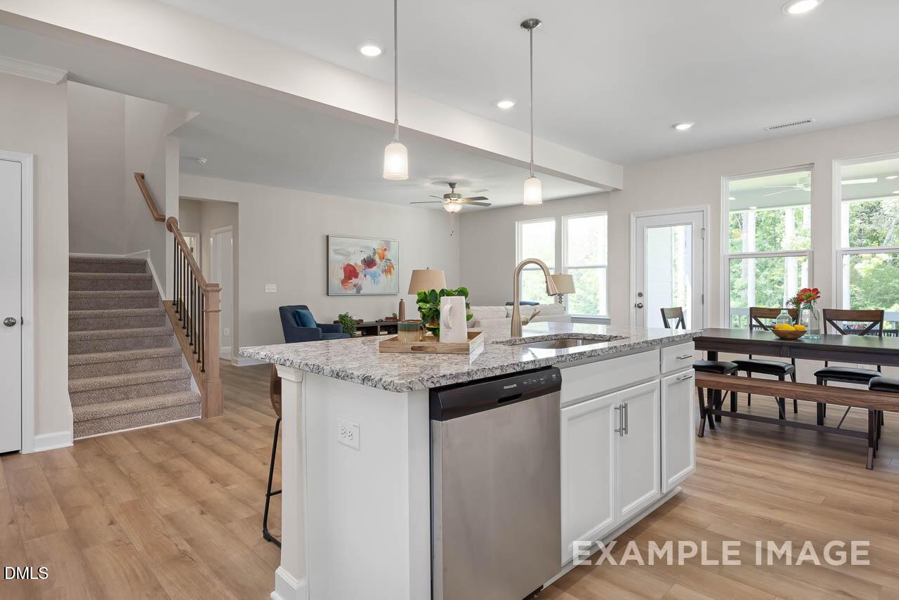Open-concept kitchen with quartz island, stainless dishwasher, white cabinets, and adjacent dining in The Willow D by Davidson Homes, Lillington, NC