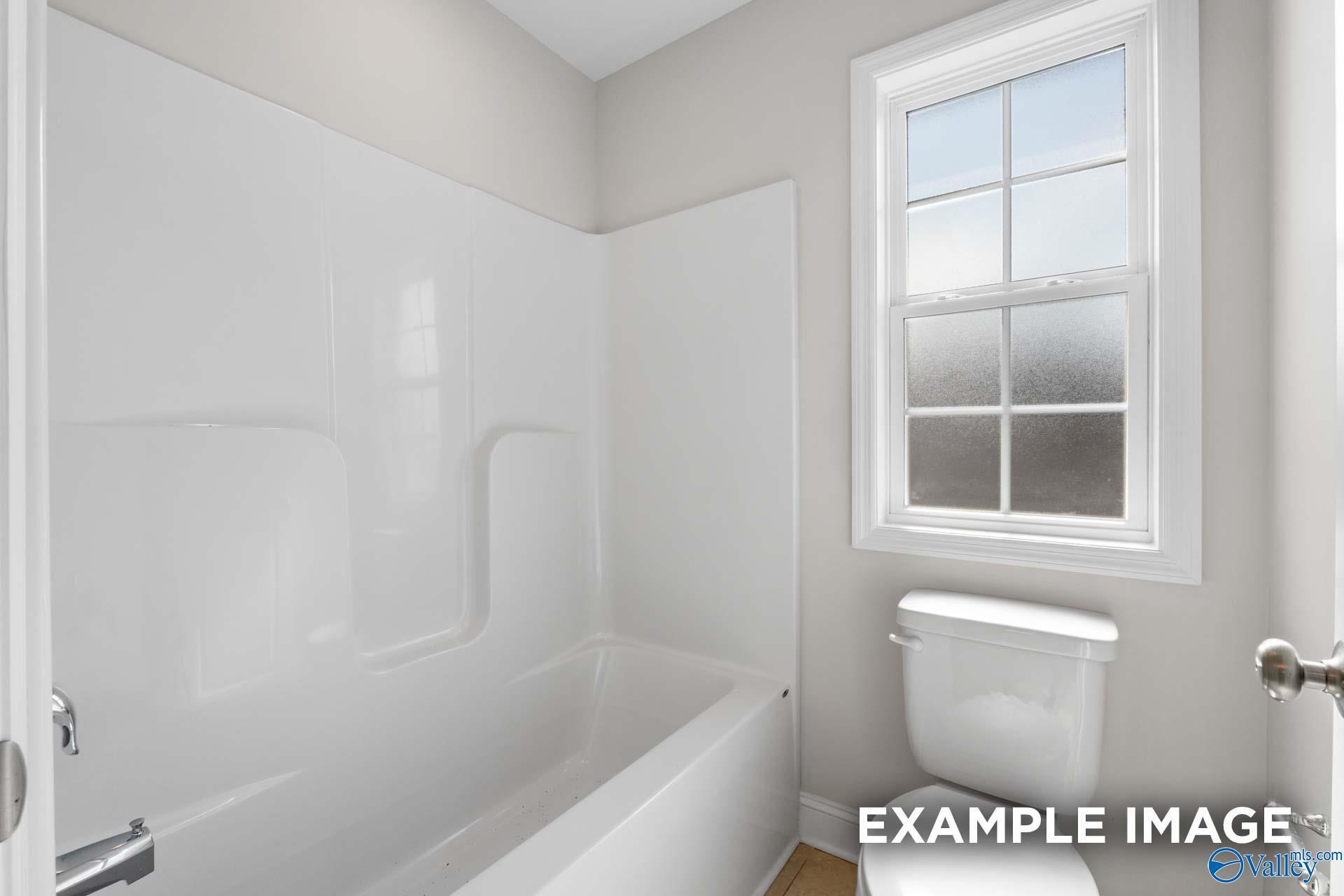 Bright bathroom featuring white tub-shower combo and toilet with frosted window in Davidson Homes Madison A, Toney, Alabama