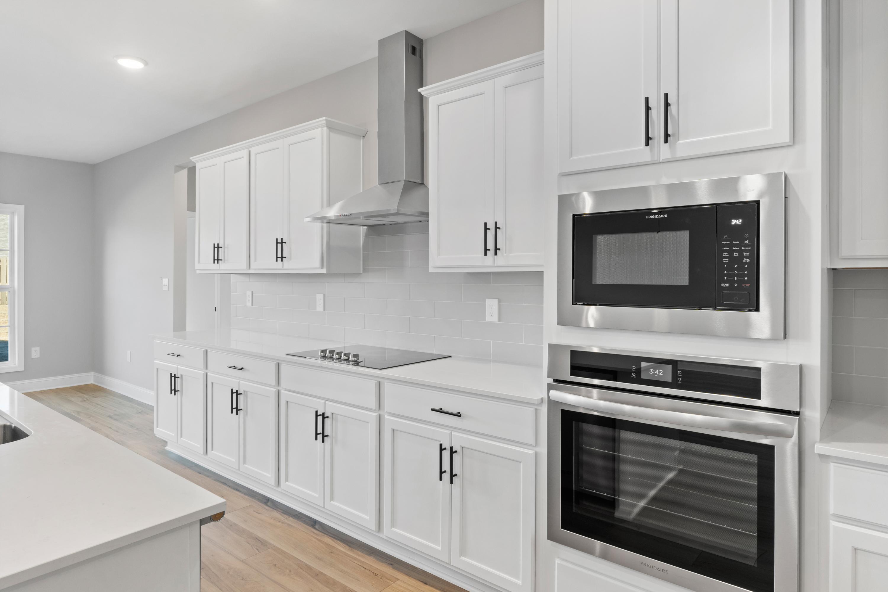 Spacious Valencia kitchen by Davidson Homes with white shaker cabinets, stainless steel appliances, large island, and hardwood floors