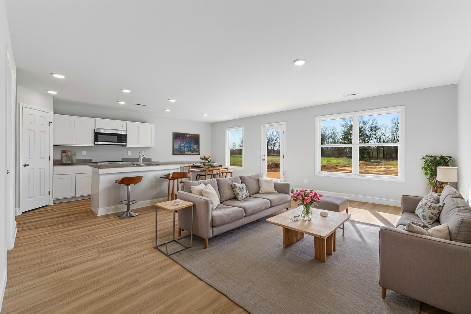 Open-concept kitchen and living room at Chapel Hill in Athens Alabama featuring white cabinetry, hardwood floors, large windows, and gray sofas