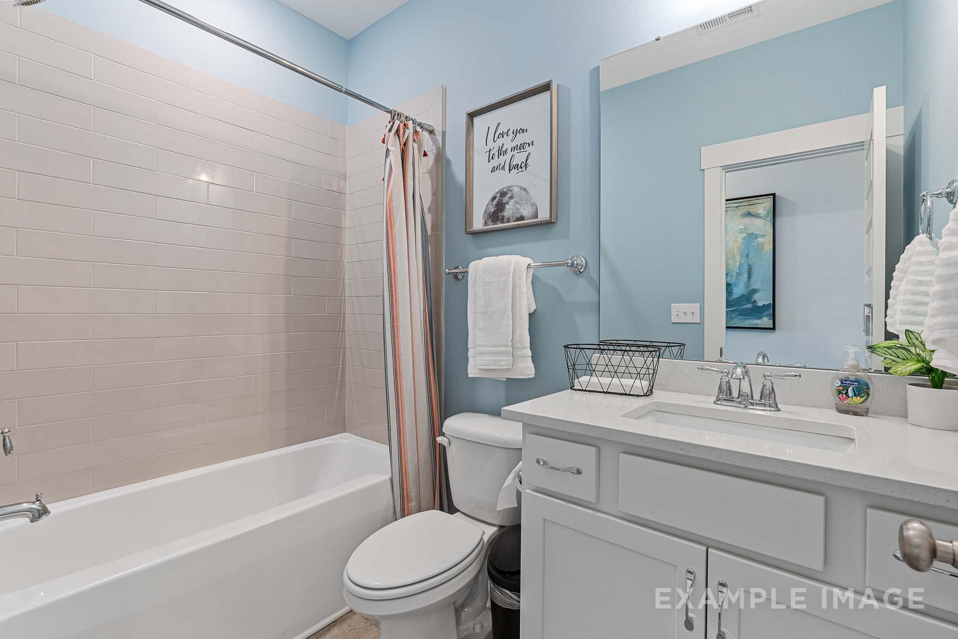Serene master bathroom in The Rockford with light blue walls, soaking tub, orange shower curtain, and white vanity sink