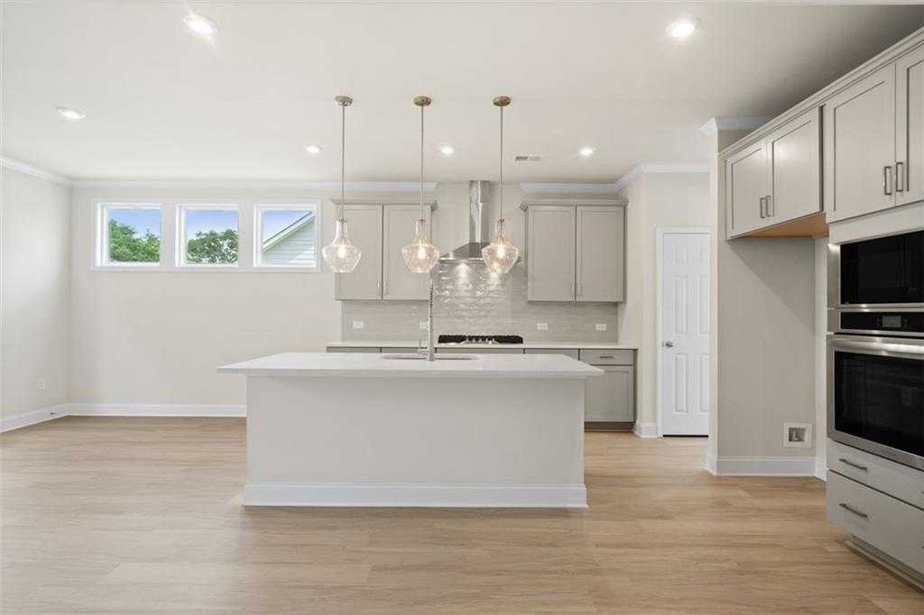 Modern open-concept kitchen with white cabinets, large island, stainless appliances in The Willow D home at Wehunt Meadows, Hoschton, GA