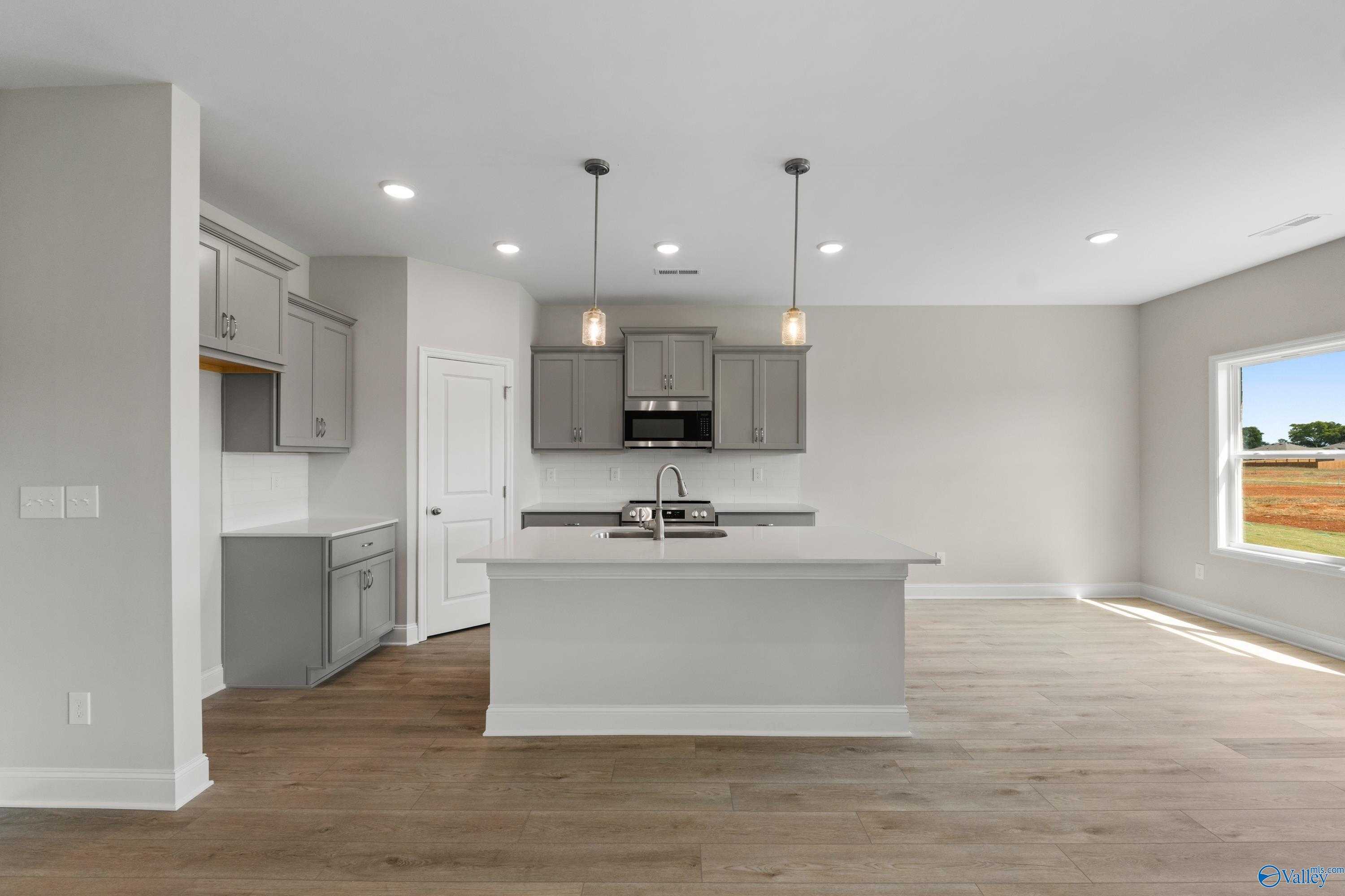 Modern kitchen featuring gray shaker cabinets, white center island sink, hardwood floors, and large window overlooking fields in Davidson Homes The Asheville, Meridianville, Alabama