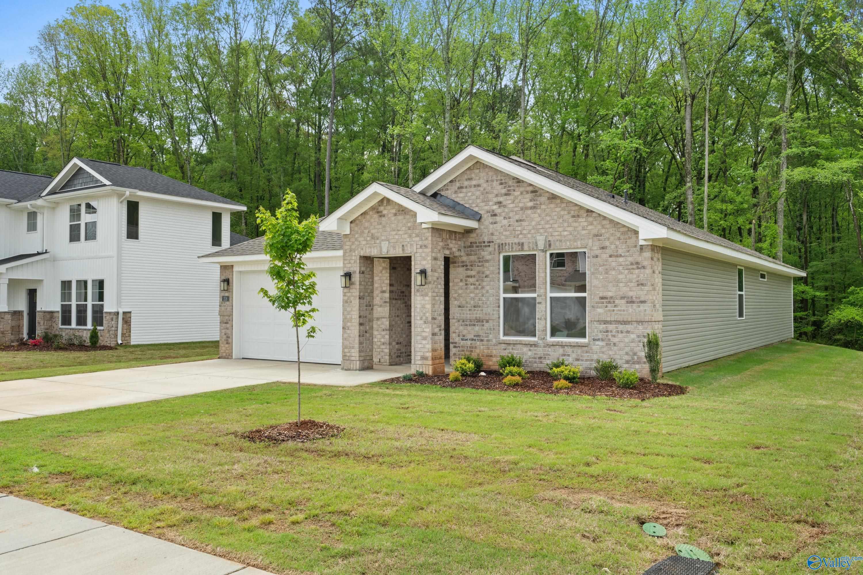 Single-story brick home with 2-car garage, front lawn, and wooded surroundings in Forest Glen, Hazel Green, Alabama by Davidson Homes The Luna