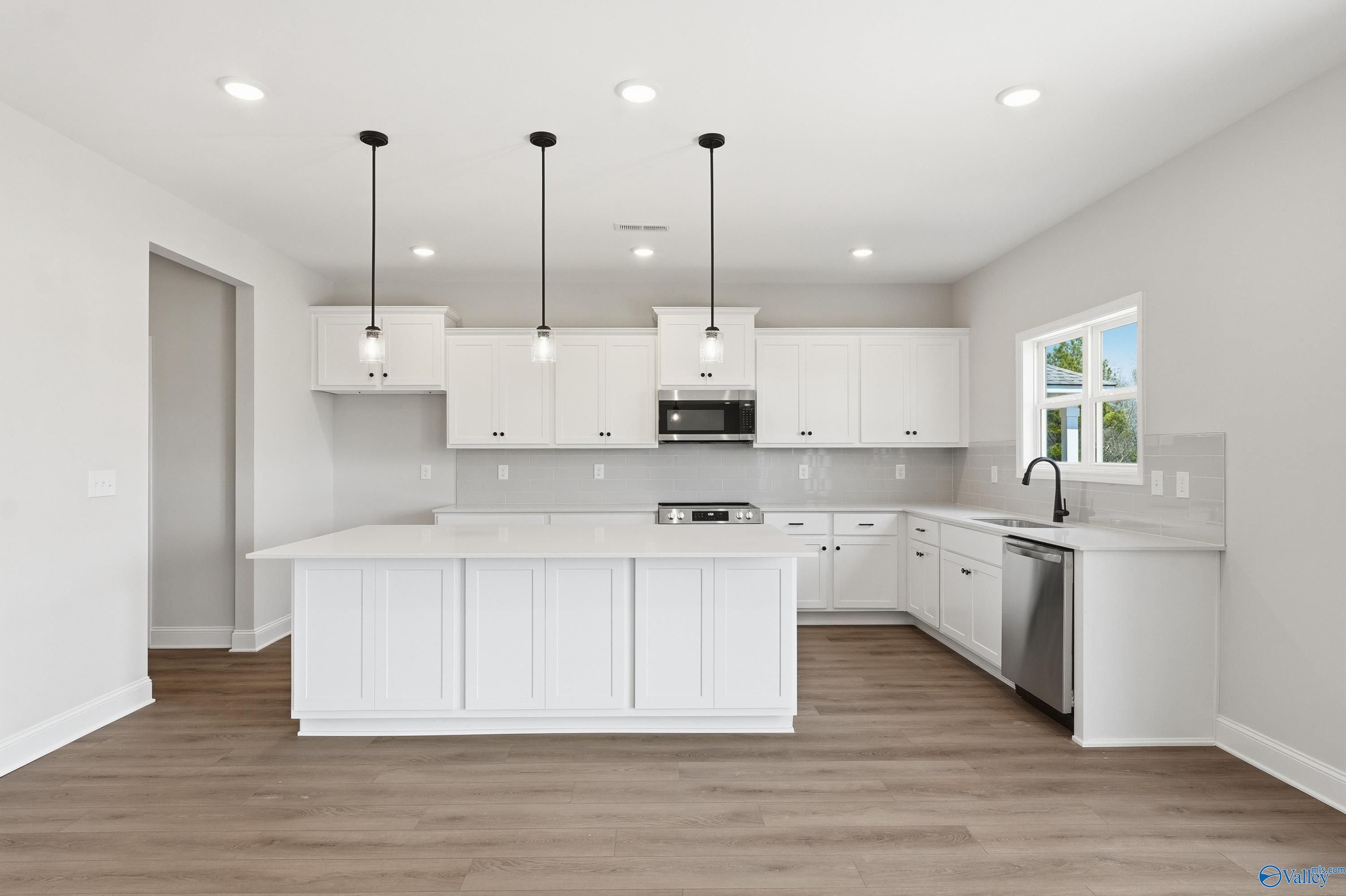 Bright modern kitchen with white shaker cabinets, quartz island, stainless appliances, and pendant lights in Davidson Homes The Chelsea D, Cullman, AL