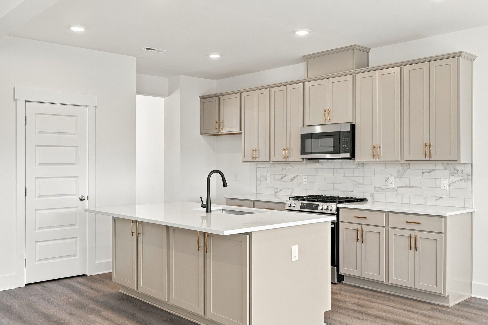 Kitchen with beige cabinetry, white quartz island, marble tile backsplash, and stainless gas range in Davidson Homes The Willow B, Gallatin TN