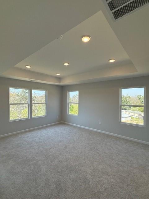 Spacious empty bedroom with gray carpet, tray ceiling, recessed lights, and large windows overlooking trees in Davidson Homes The Durham B, Cumming, Georgia