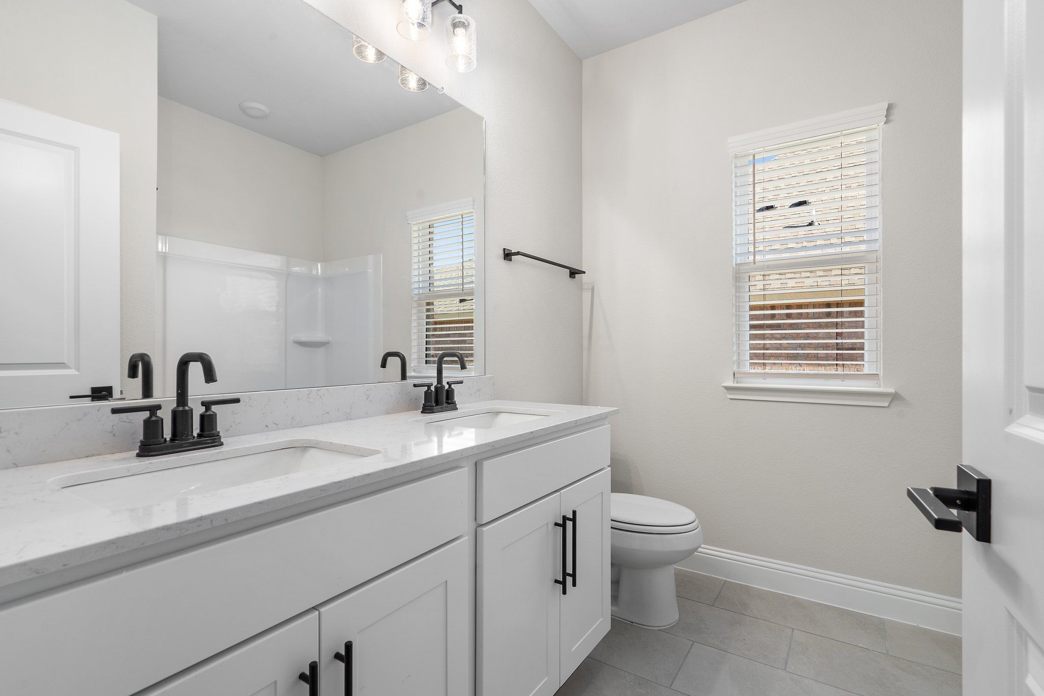 Spacious bathroom in The Holly F design featuring a white dual-sink vanity, modern matte black fixtures, and tiled floors.