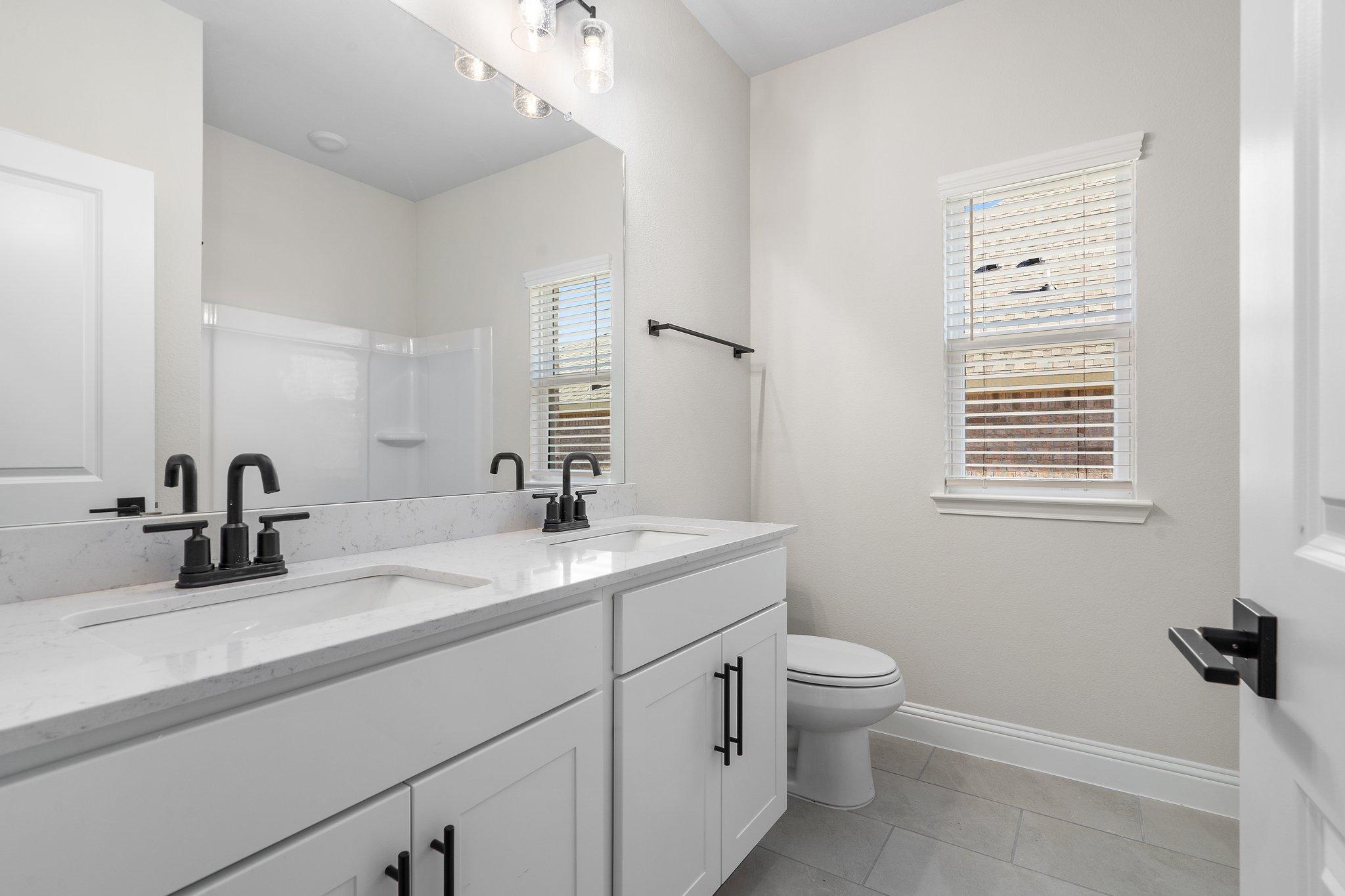 Spacious bathroom in The Holly F design featuring a white dual-sink vanity, modern matte black fixtures, and tiled floors.