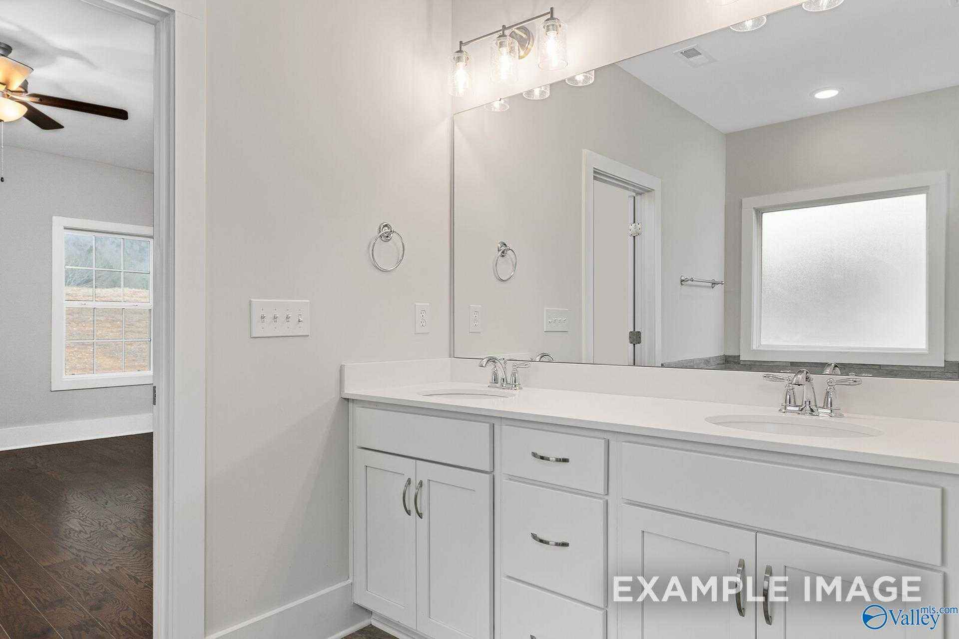 Modern master bathroom featuring double white vanity, mirrors, and frosted window in Davidson Homes The Rockford, Harvest, AL