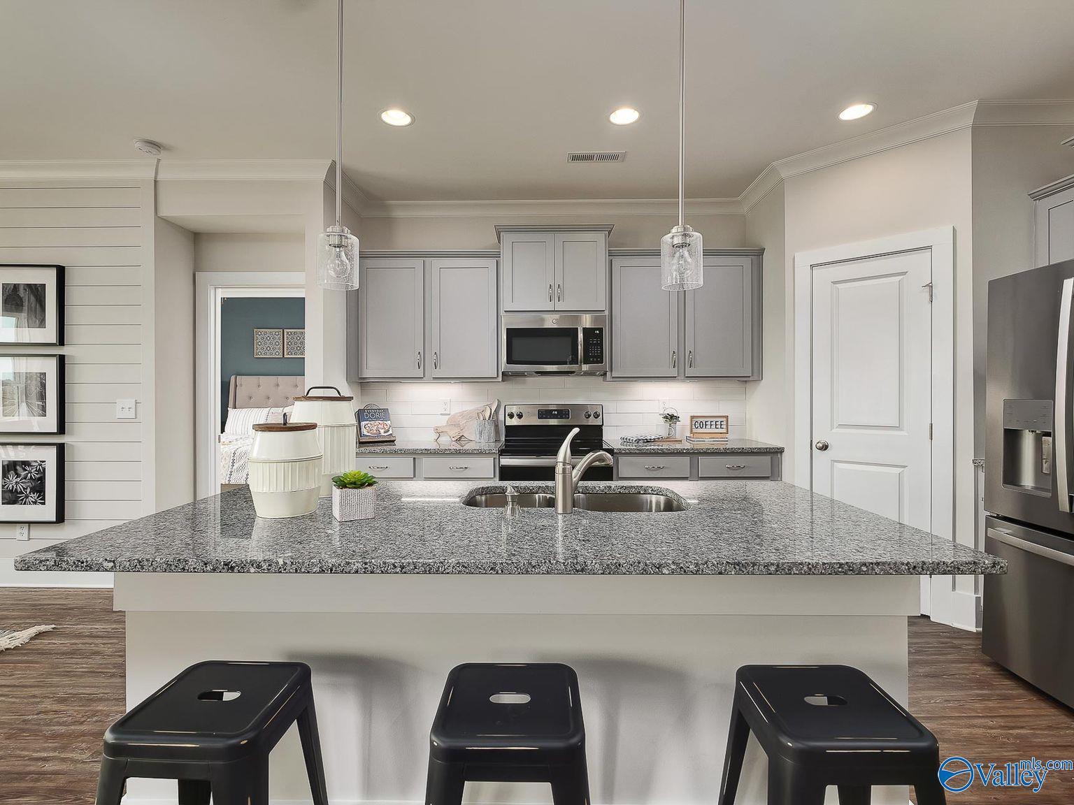 Open-concept kitchen with granite island, stainless steel appliances, and gray cabinets in Davidson Homes The Everett, Toney, Alabama