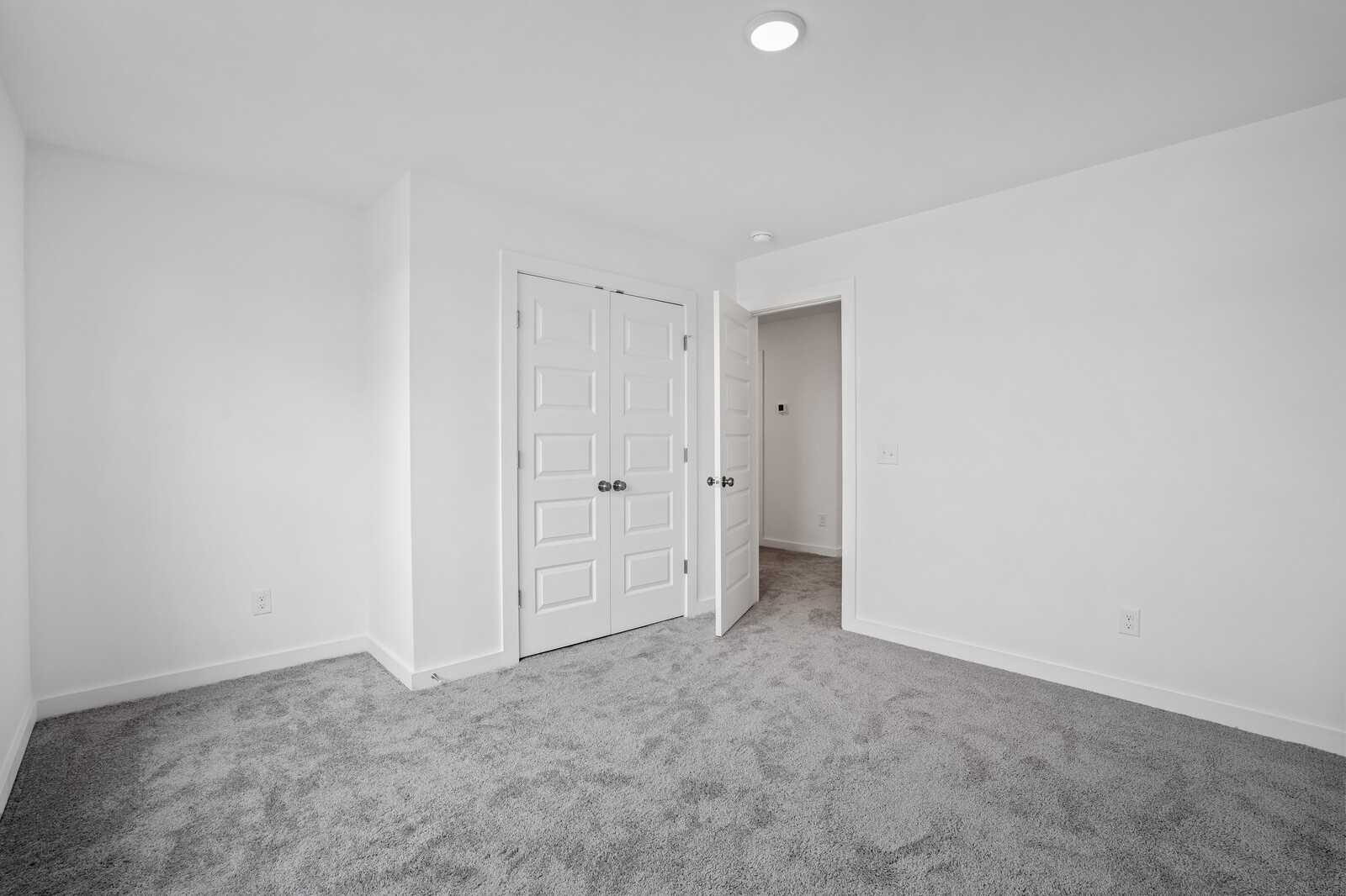 Spacious empty bedroom featuring gray carpet, white walls, and double doors in Davidson Homes The Logan B, Calista Farms, White House, TN