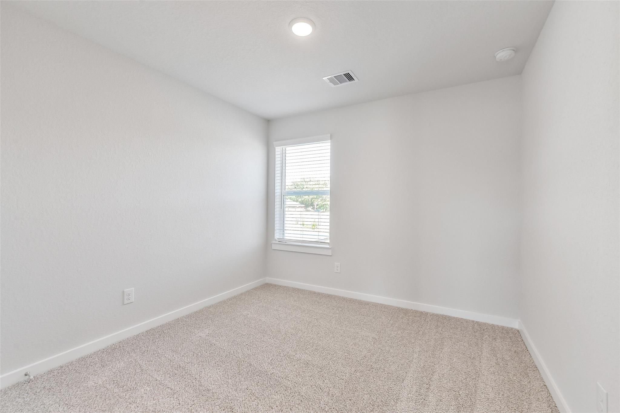 Bright secondary bedroom with beige carpet, white walls, and window blinds in Davidson Homes The Blanco E, Magnolia, Texas