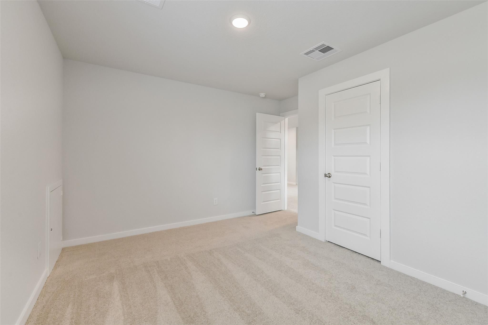 Bright secondary bedroom with light gray walls, beige carpet, and adjacent hallway in The Brazos E by Davidson Homes, Cleveland, TX