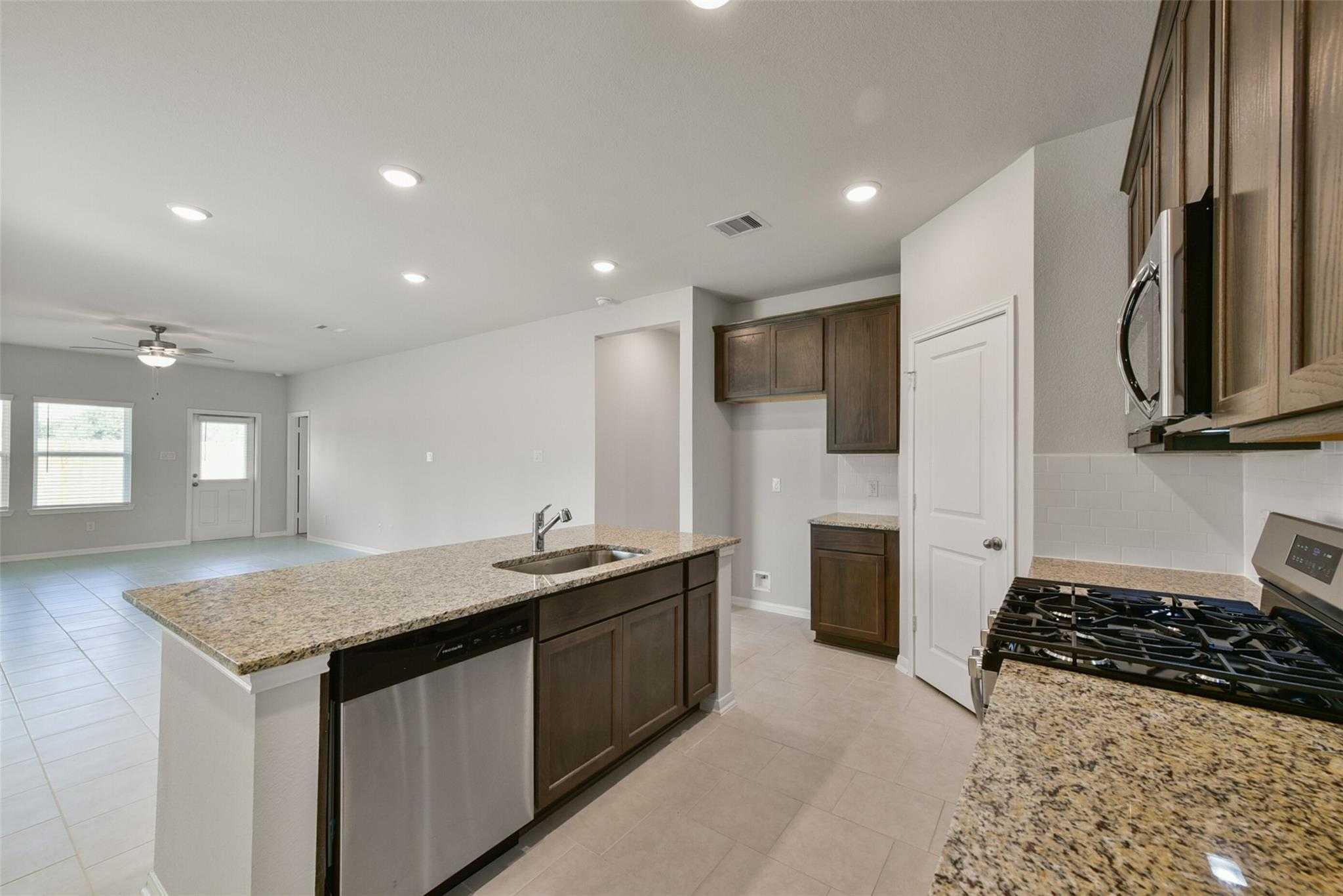 Modern open-concept kitchen with granite island, stainless steel appliances, and shaker cabinets in The Sabine E home, Dayton Texas