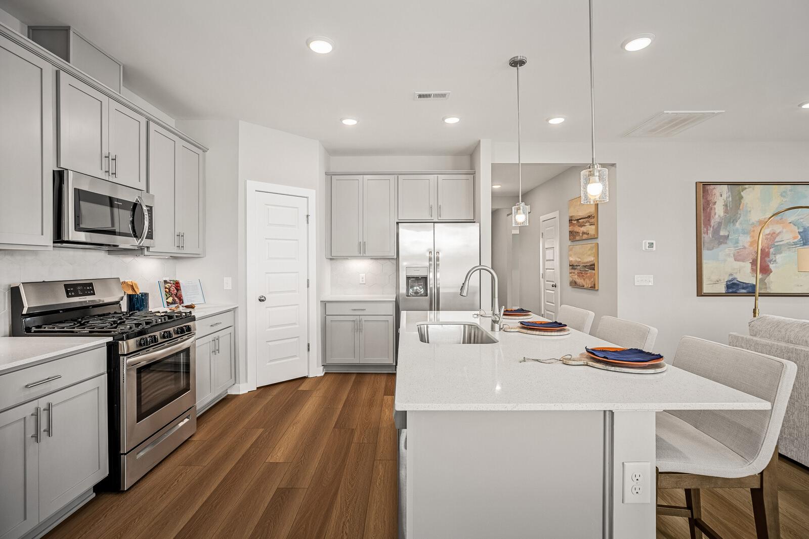 Spacious modern kitchen at Sage Farms in White House TN with white cabinets, quartz island, stainless appliances, and hardwood floors