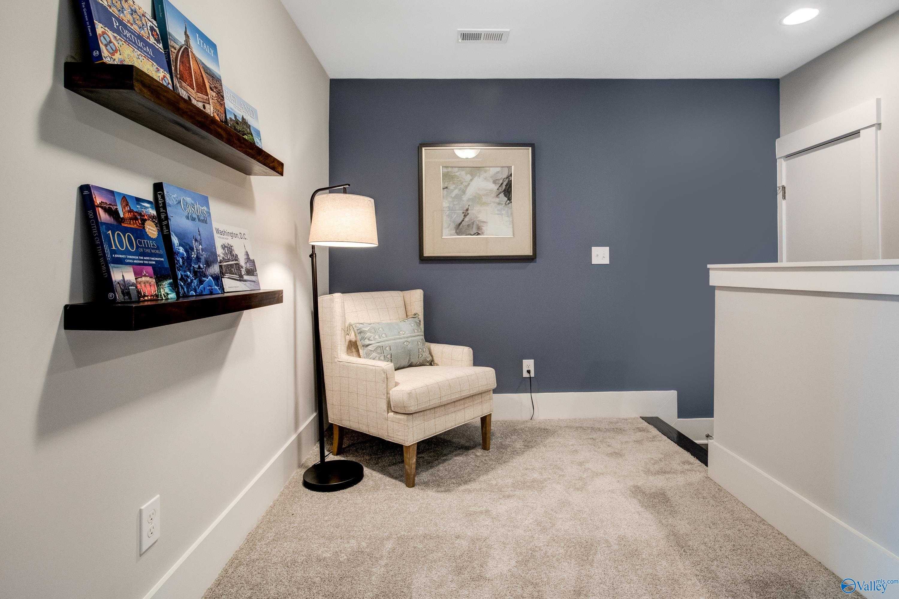 Cozy loft reading nook with blue accent wall, floating bookshelves, armchair, lamp in The Covington C, Decatur, Alabama