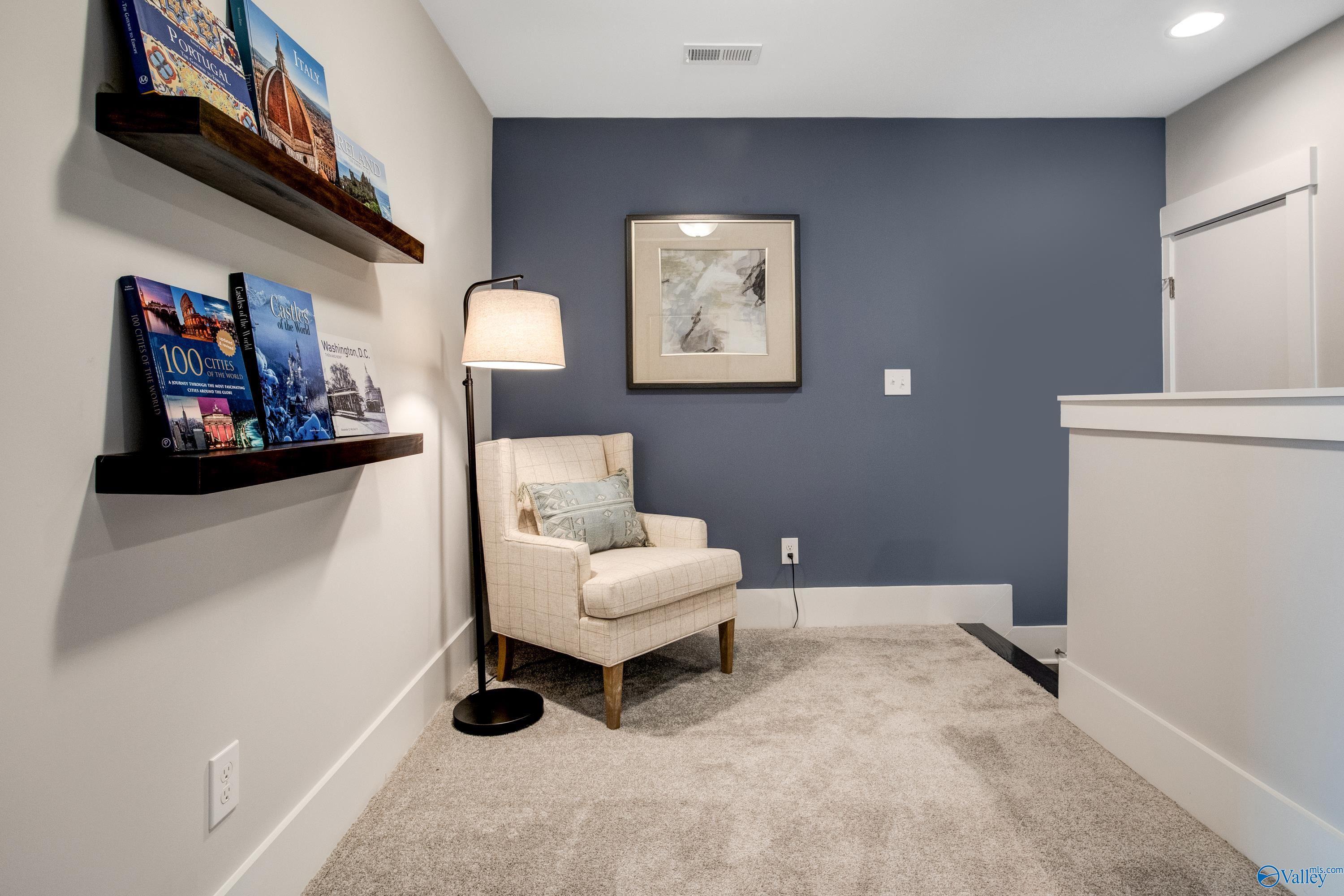 Cozy loft reading nook with blue accent wall, floating bookshelves, armchair, lamp in The Covington C, Decatur, Alabama