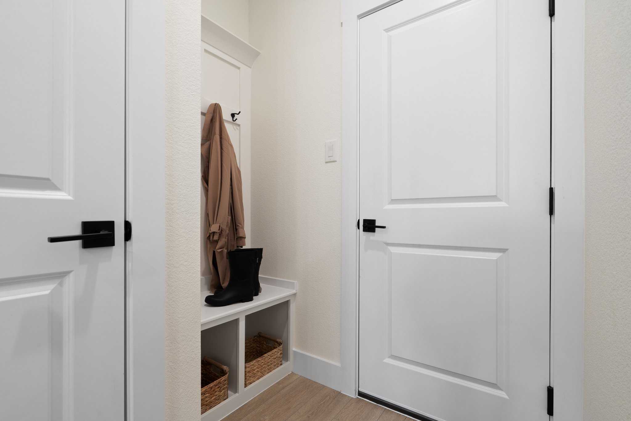Functional mudroom in The Wake by Davidson Homes featuring white paneled doors, built-in bench with boots, hanging coat, and storage baskets