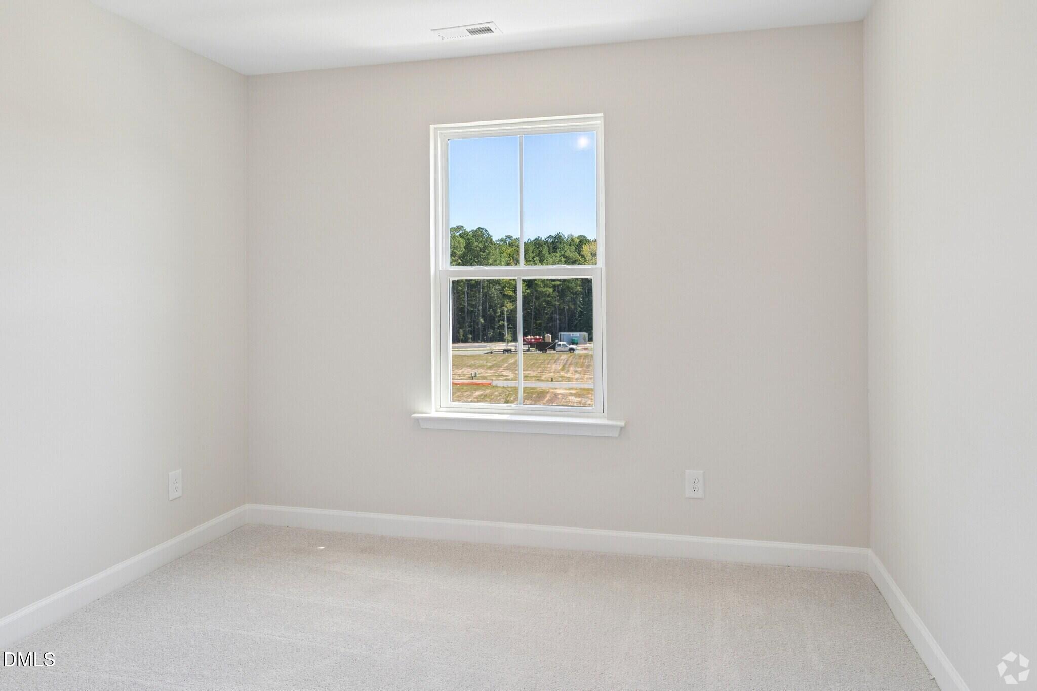Bright empty bedroom with carpet, neutral walls, and double-hung window overlooking trees in Davidson Homes The Mitchell, Knightdale NC