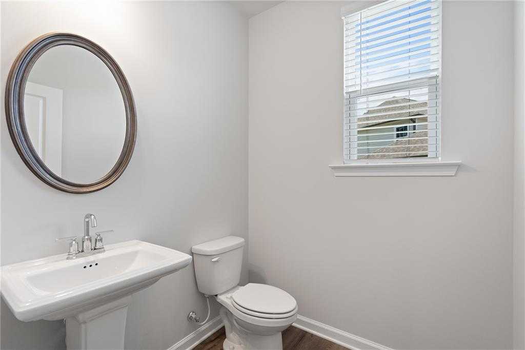 Bright powder room with pedestal sink, round mirror, white toilet, and window blinds in Davidson Homes The Hickory B, Winder, Georgia